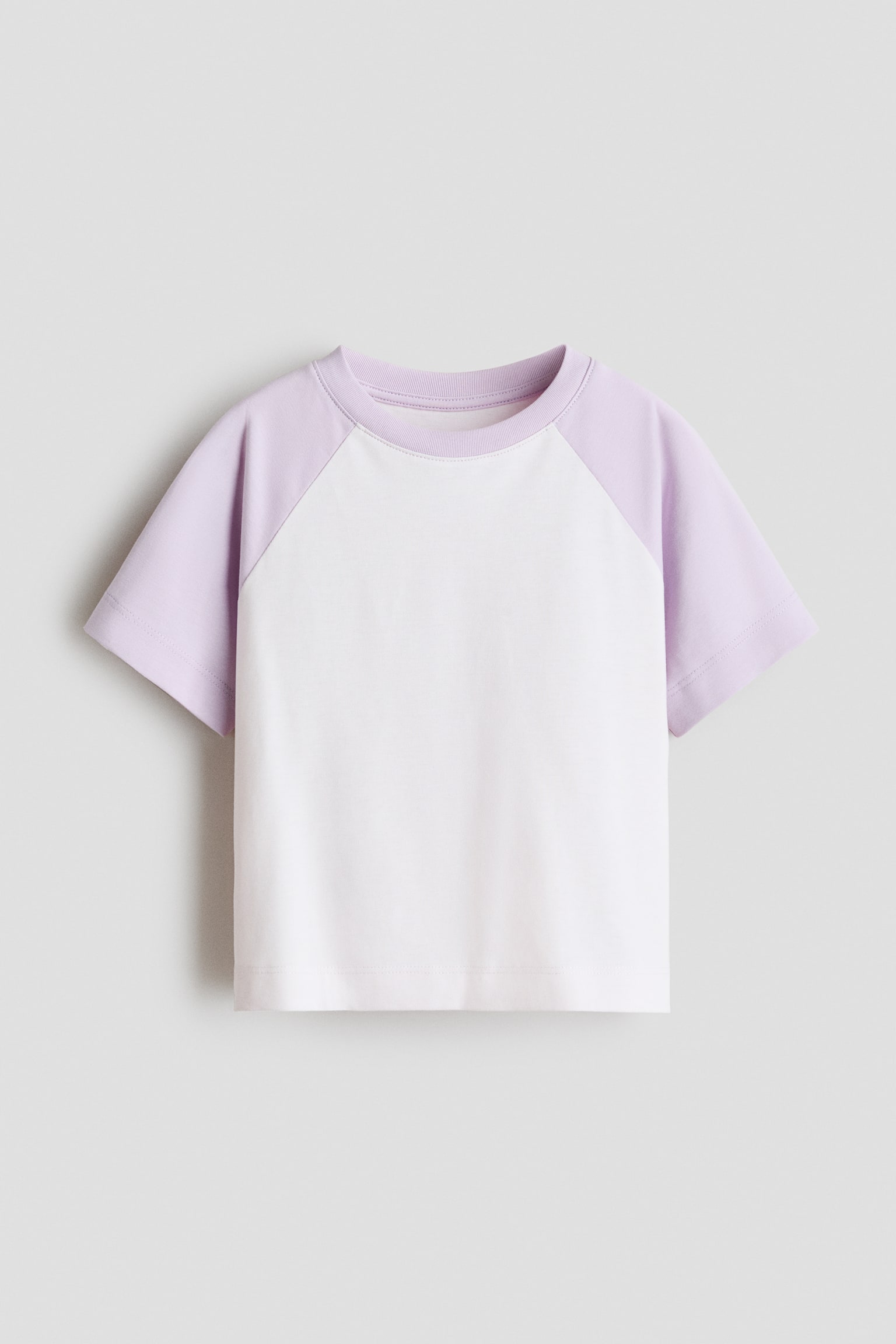 A short-sleeved raglan t-shirt is shown from the front, featuring a white body and light purple sleeves. The t-shirt has a matching purple ribbed crew neck and a straight hem.