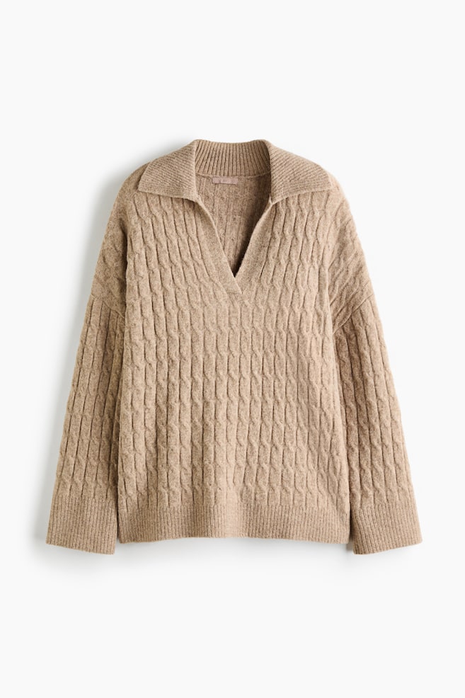 The beige cable-knit sweater is facing front, showcasing a relaxed fit with a polo collar and an open V-neckline. It is featuring dropped shoulders, long sleeves with wide ribbed cuffs, and a matching ribbed hem. - 1