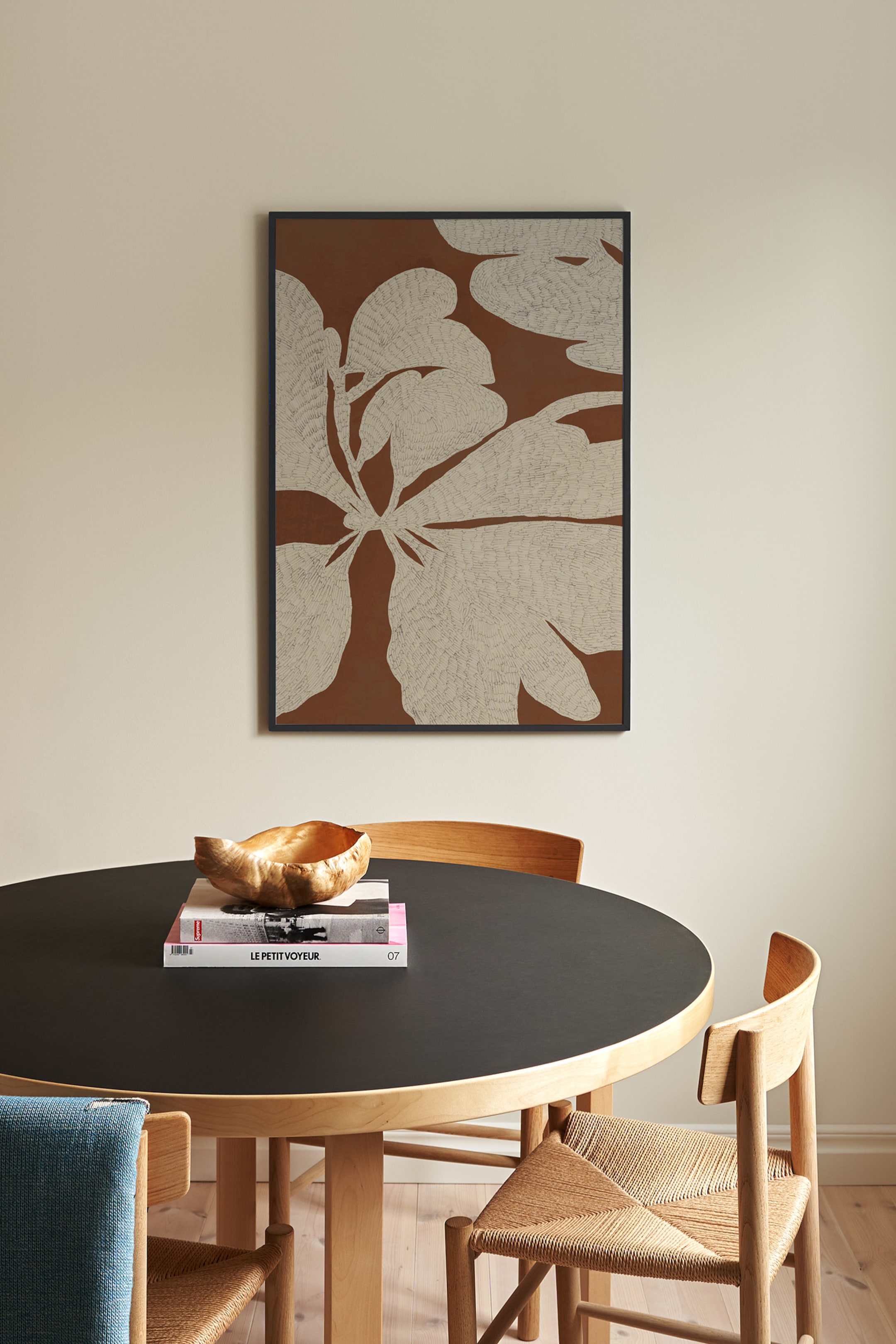 Se større billede: Et rektangulært indrammet kunsttryk viser et stiliseret botanisk mønster af store, teksturerede beige blade med fine, skitserede detaljer mod en ensfarvet varm brun baggrund. Kunstværket hænger lodret og er indrammet i en slank, sort minimalistisk ramme.