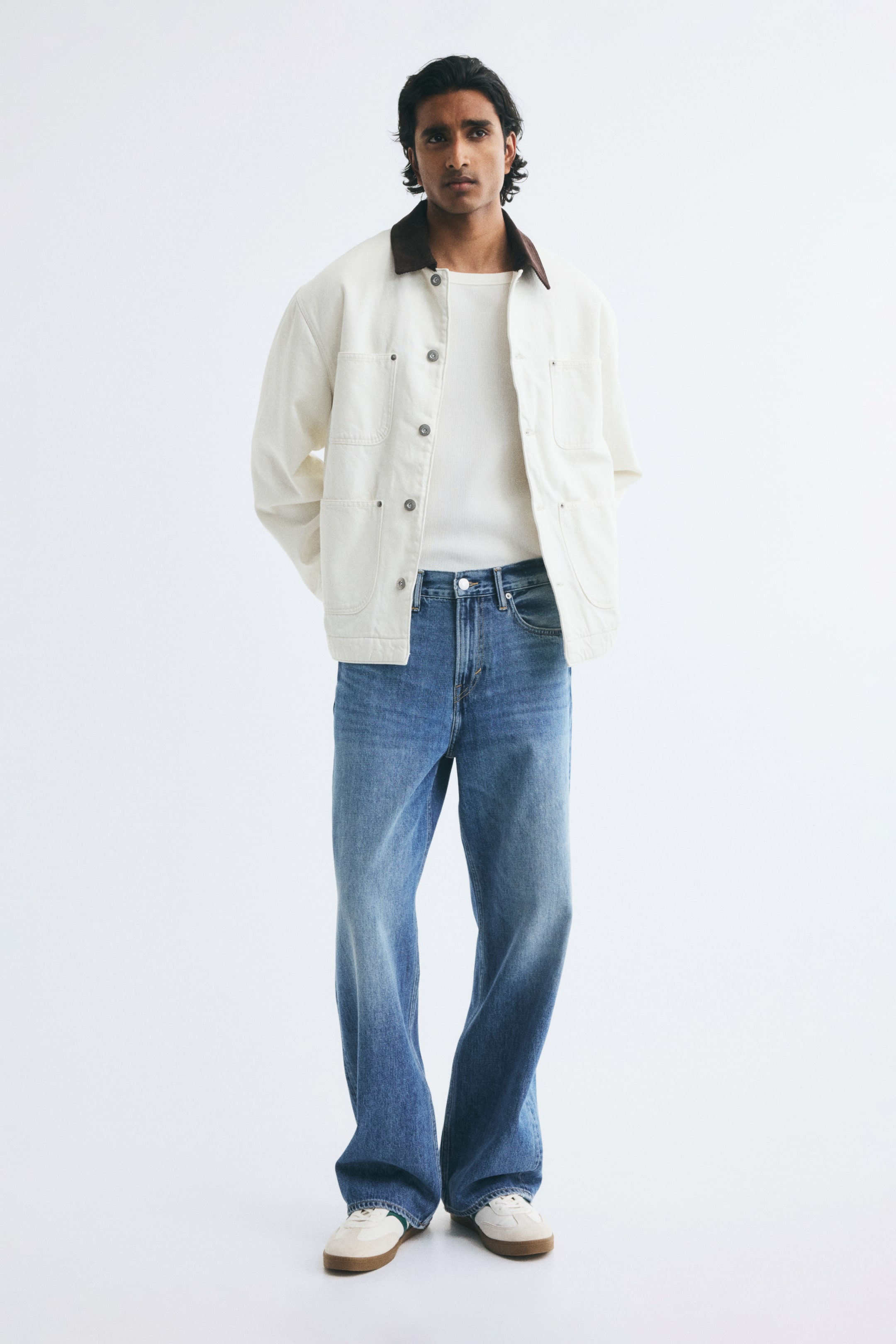 View larger image: Blue denim jeans in a loose, straight-leg fit are being worn by the model, styled with a tucked-in white top, an open off-white jacket, and sneakers. The jeans feature a medium-blue wash with light fading along the thighs and a relaxed drape that pools slightly at the hem.