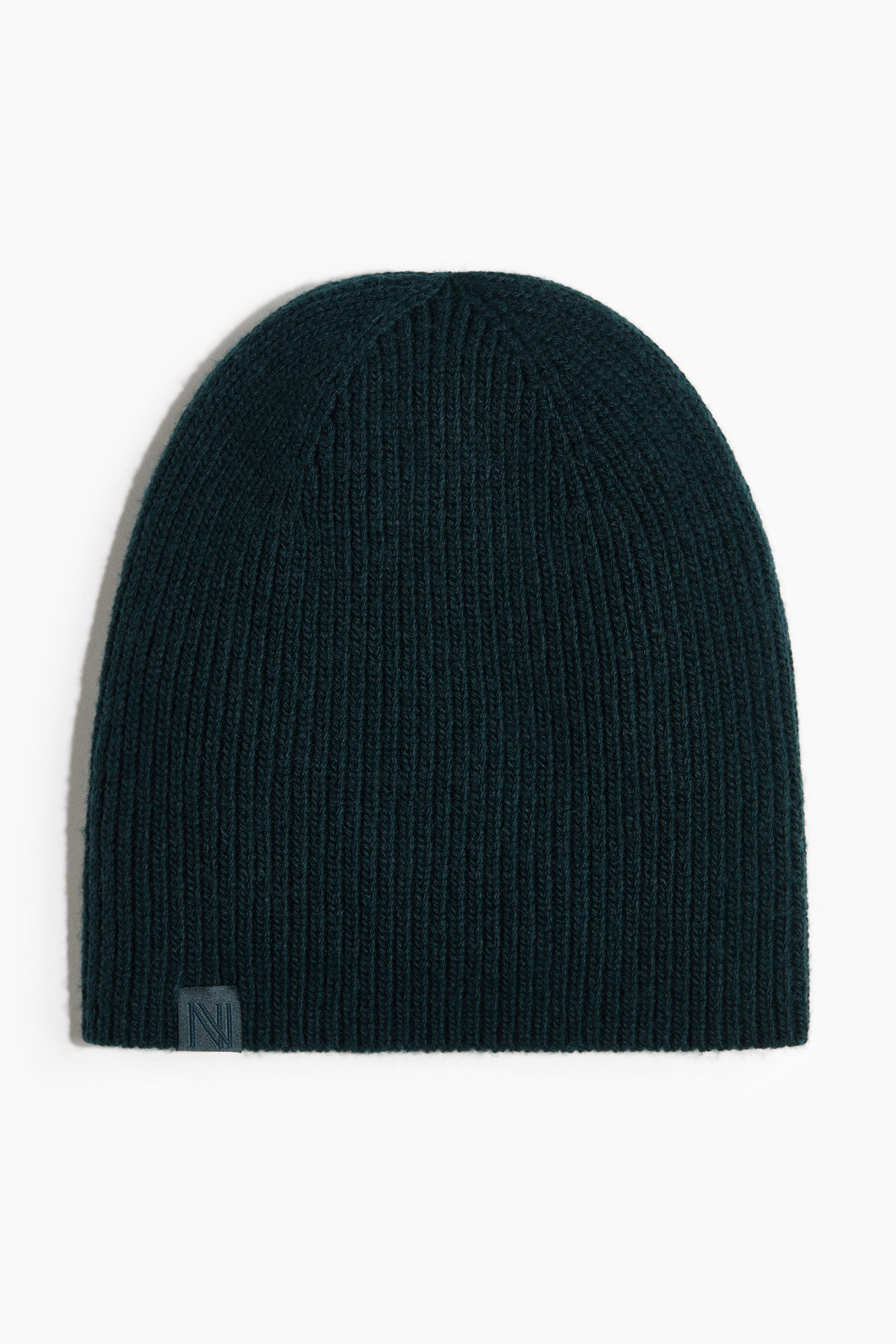 Größeres Bild anzeigen: Eine dunkelgrüne, gerippte Strickmütze ist von vorne zu sehen. Ein kleines, quadratisches Etikett in derselben dunkelgrünen Farbe, mit einem eingeprägten Buchstaben N, ist auf der unteren linken Vorderseite sichtbar.