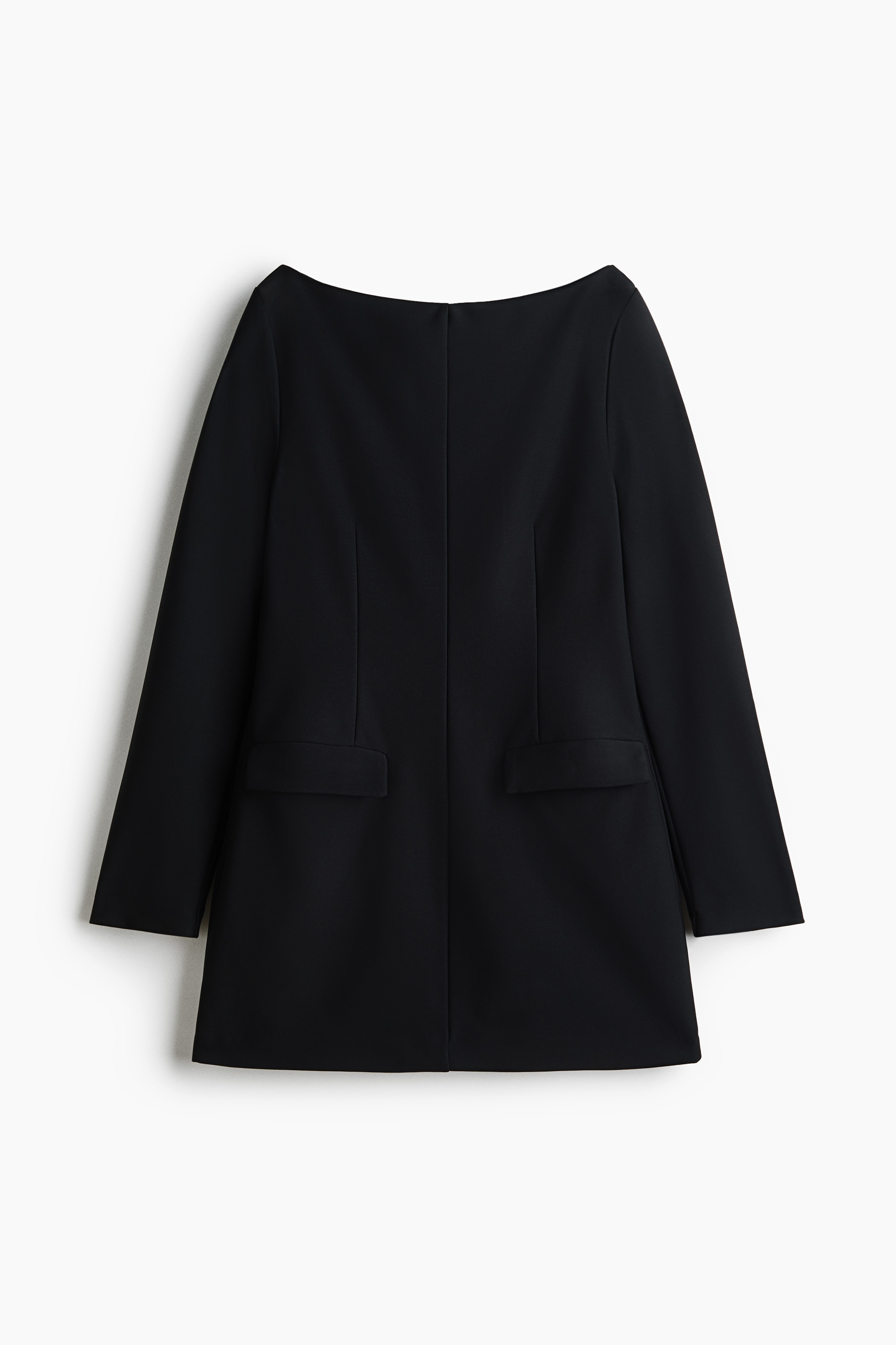 A short black stretch-jersey dress with a boat neckline, long sleeves, waist darts and front flap pockets is worn by the model. The outfit is styled with black stirrup leggings and pointed-toe heels, with a small black clutch held in one hand.