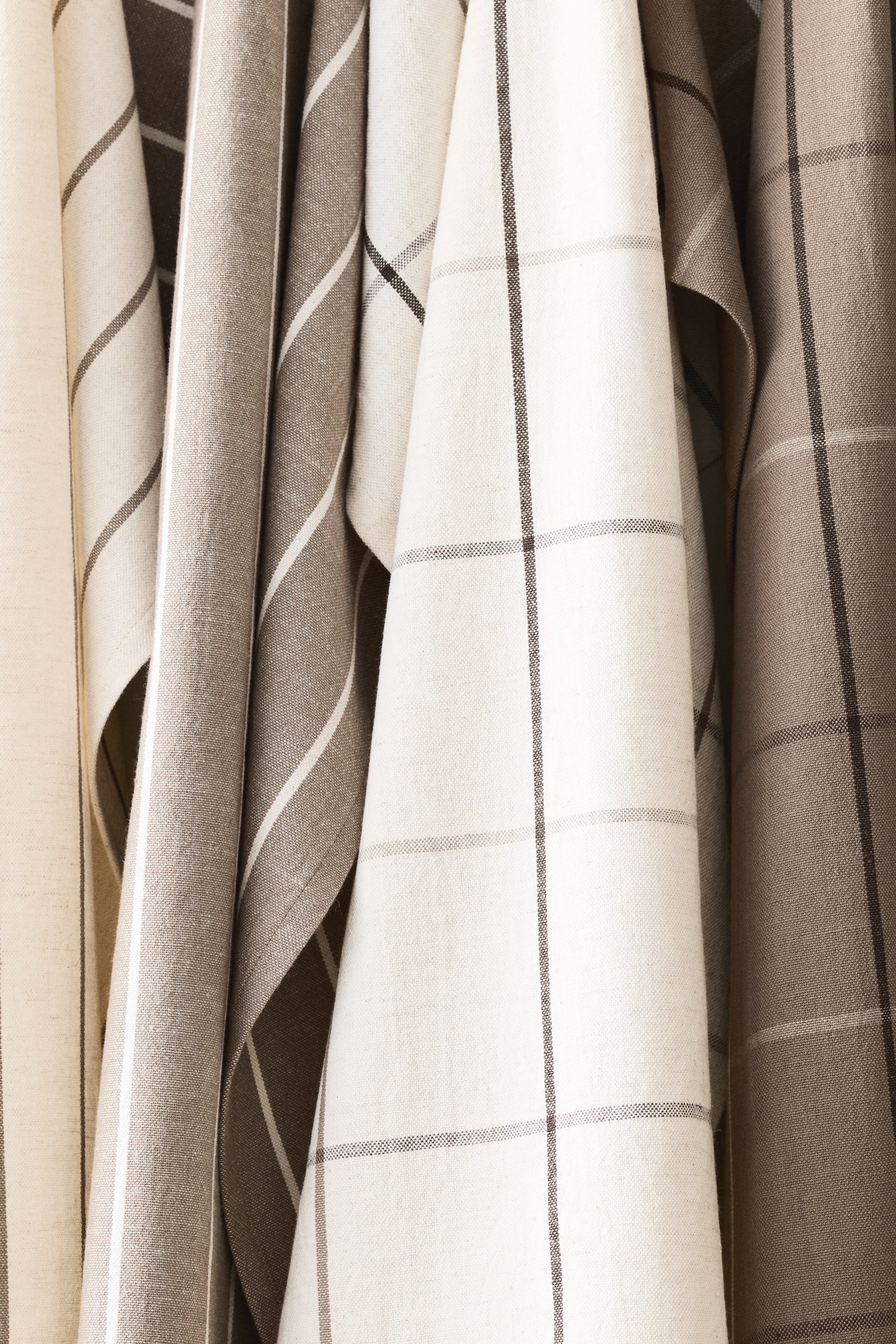 View larger image: Tea towels crafted from a cotton and linen blend showcase a range of yarn-dyed patterns, featuring stripes and checks, in neutral hues of off-white, cream, and earthy greys and browns.