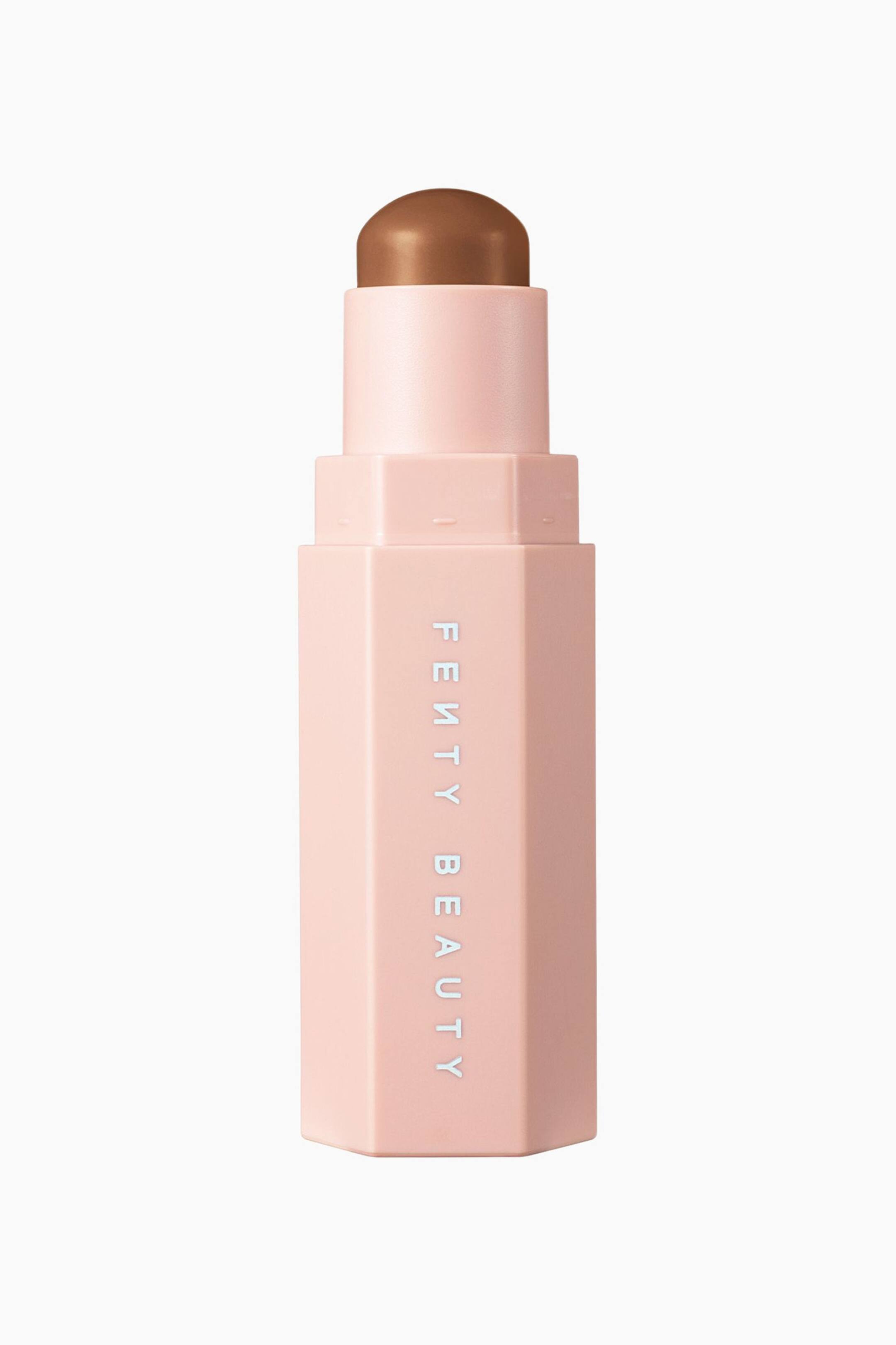 Visa större bild: En contour stick i ett ljusrosa, sexkantigt hölje står lodrätt och visar varumärkesnamnet "FENTY BEAUTY" tryckt vertikalt i vitt på framsidan. Höljet är öppet, med ett cylindriskt innerrör som sträcker sig uppåt för att visa en kupolformad contour-produkt i mediumbrun kräm.