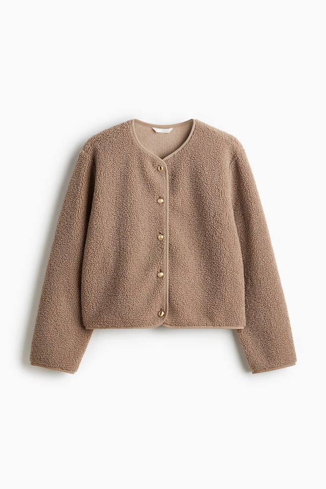 Una chaqueta de peluche color topo de ajuste holgado se presenta desde el frente. Presenta un escote redondo y un ribete estrecho que sigue el escote, la abertura frontal y el dobladillo. Botones de metal en tono dorado abrochan la chaqueta por el centro del frente. - 1