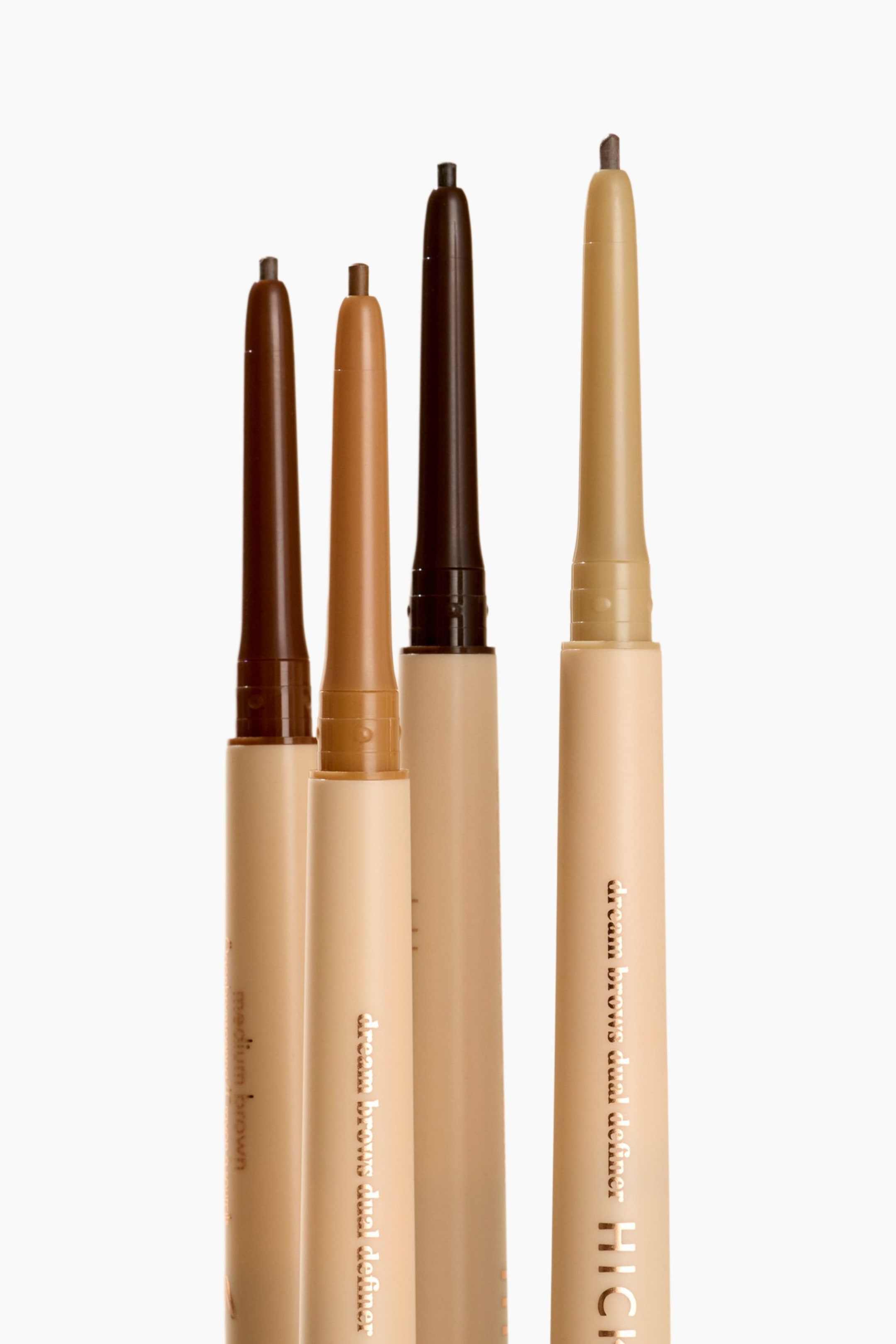 Se større billede: Fire dobbelte øjenbrynsdefinerer står oprejst, let vinklet fra fronten, hver med en lys beige base og en tilspidset top. Mejsel-formede defineringsspidser er synlige i nuancer af lys, mellem- og mørkebrun, med teksten "dream brows dual definer" synlig på siden af nogle produkter.