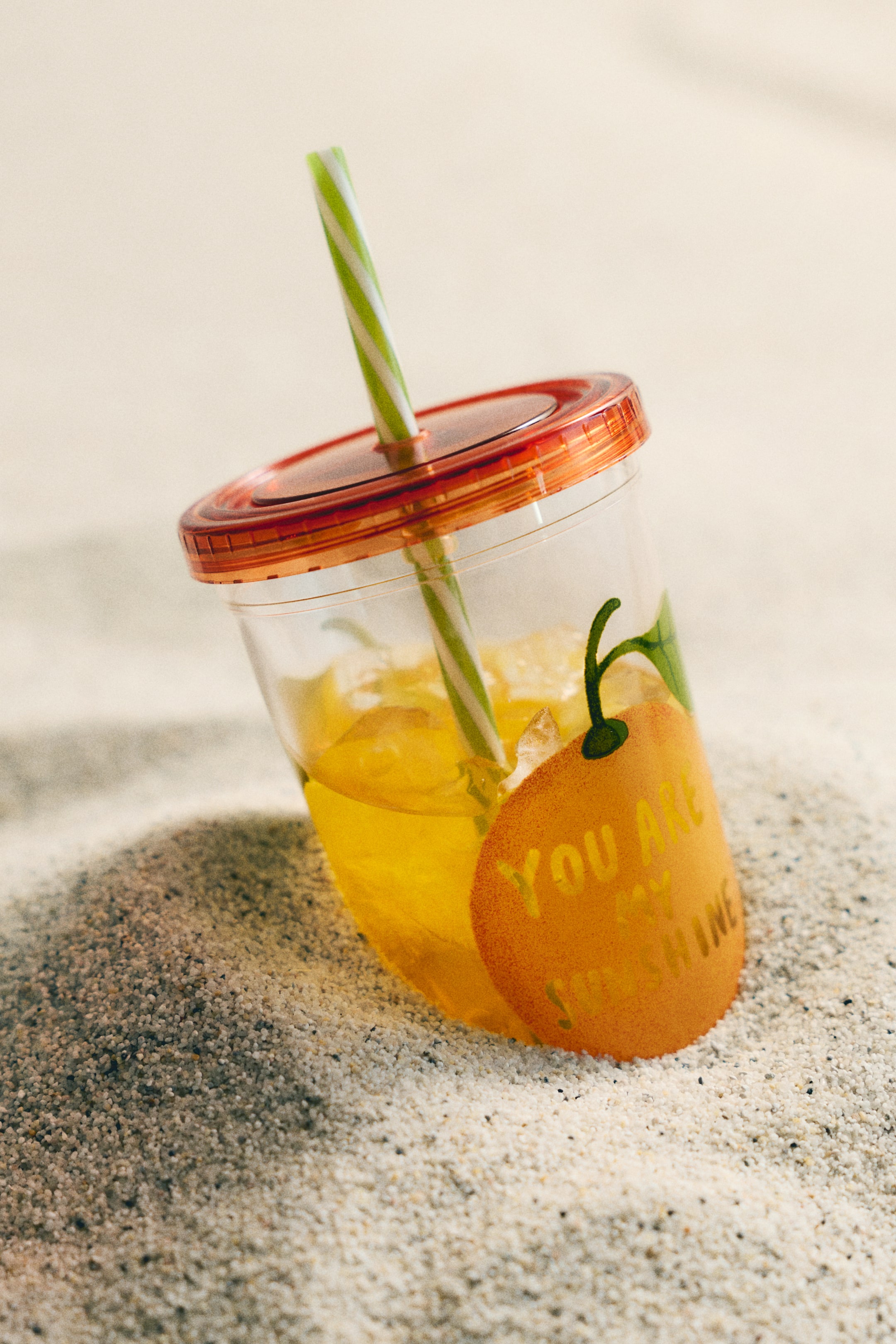 Grotere afbeelding bekijken: Een transparante plastic mok met een zijprint van een sinaasappelontwerp met de tekst 'YOU ARE MY SUNSHINE', gevuld met gele vloeistof en ijs. De mok heeft een bovenste diameter van 9 cm en een hoogte van 13 cm, en is voorzien van een oranje schroefdeksel en een groen-wit gestreept rietje.
