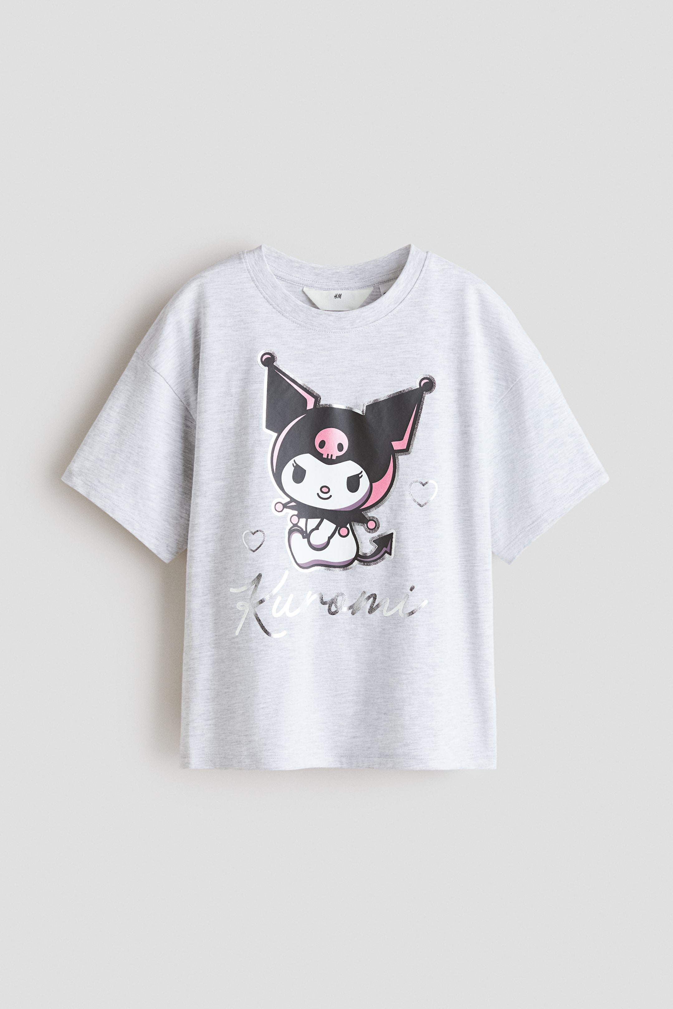 拡大画像を表示: ライトグレーの杢Tシャツのフロント。リブ仕上げのラウンドネックと、ゆるやかに落ちたショルダーが特徴です。フロント中央には、黒い耳とピンクのディテール、スカルモチーフをあしらったKuromiキャラクターのグラフィックプリントが配置され、メタリックシルバーの「Kuromi」ロゴが添えられています。