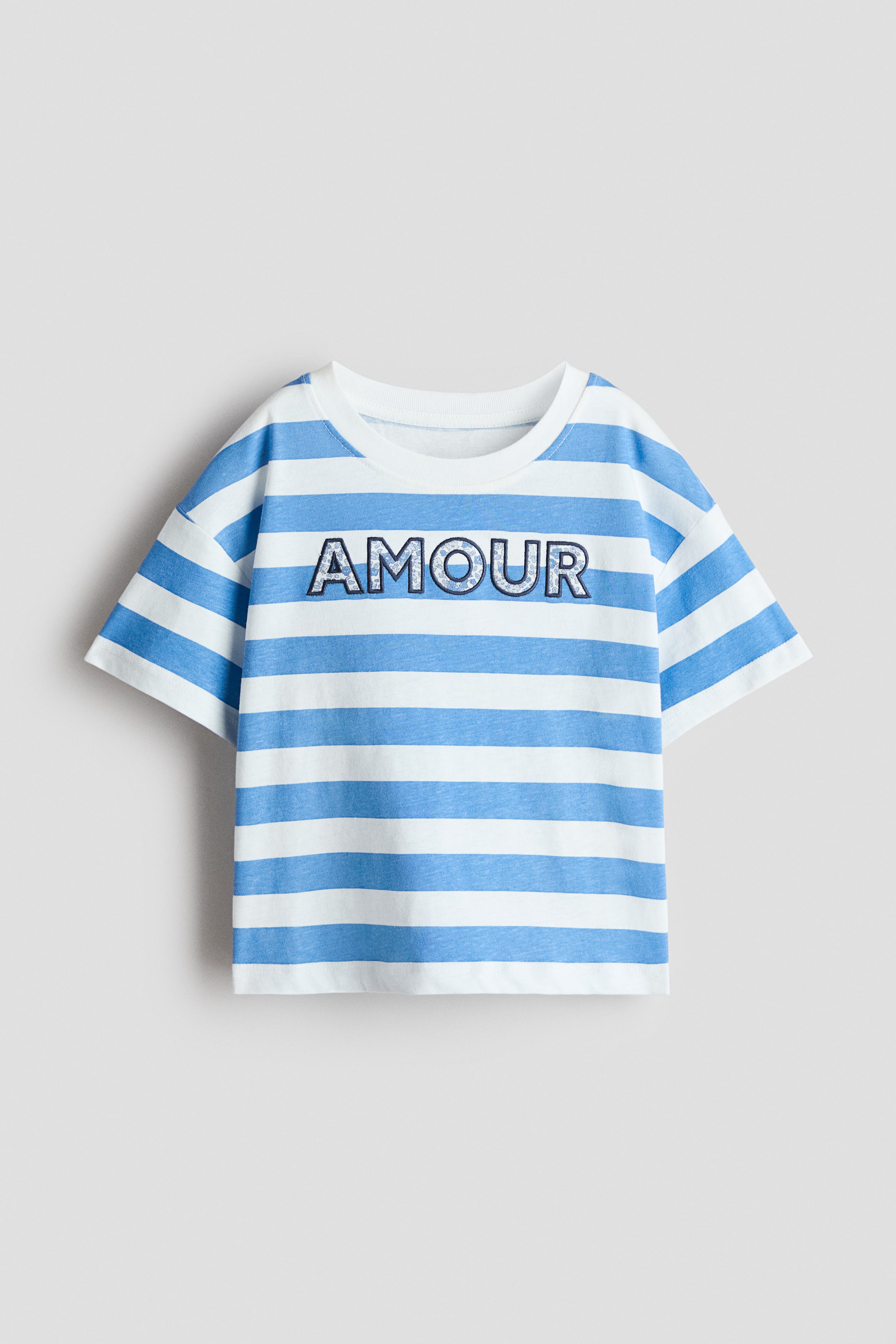View larger image: A relaxed-fit, embellished T-shirt is showcasing its FRONT, adorned with white and light blue horizontal stripes, a ribbed trim around the neckline, and low dropped shoulders. The word 'AMOUR' is prominently displayed on the chest, highlighted with a dark outline and a shimmering fill.