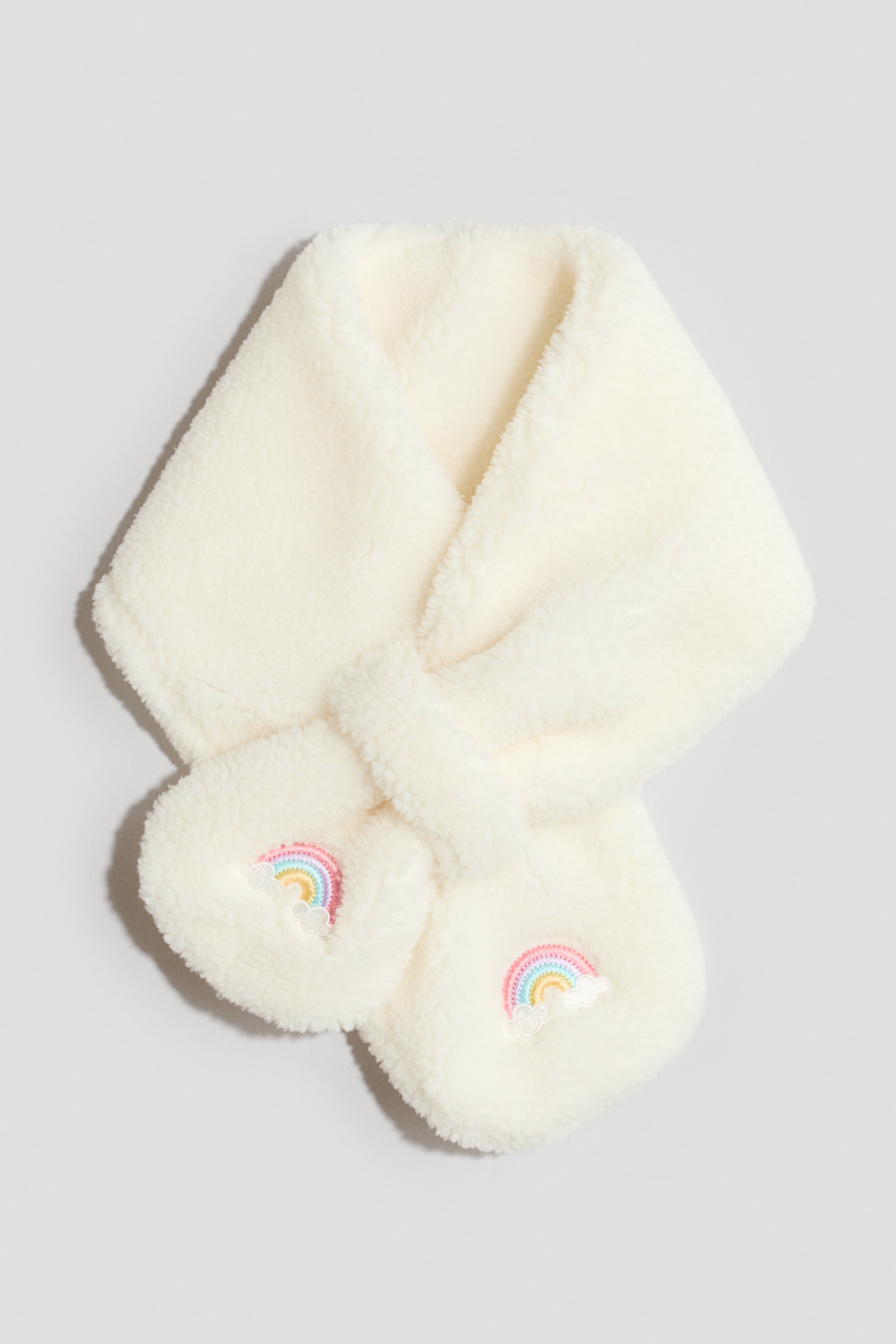 Größeres Bild ansehen: Frontansicht eines cremeweißen, flauschigen Kunstfellschals mit Durchziehschlaufendesign. Bunte aufgestickte Regenbögen mit weißen Wolken verzieren beide abgerundeten Enden.