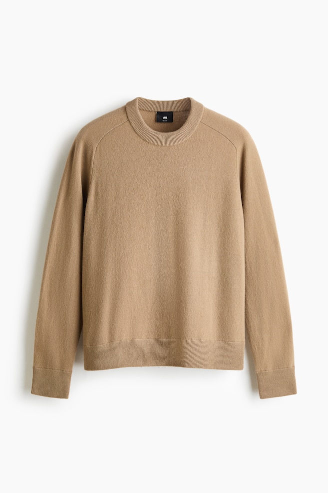 A beige knitted jumper is facing front, showcasing a ribbed crew neck, raglan long sleeves, and a ribbed hem and cuffs. The garment presents a soft, fine-knit texture and a relaxed silhouette. - 1