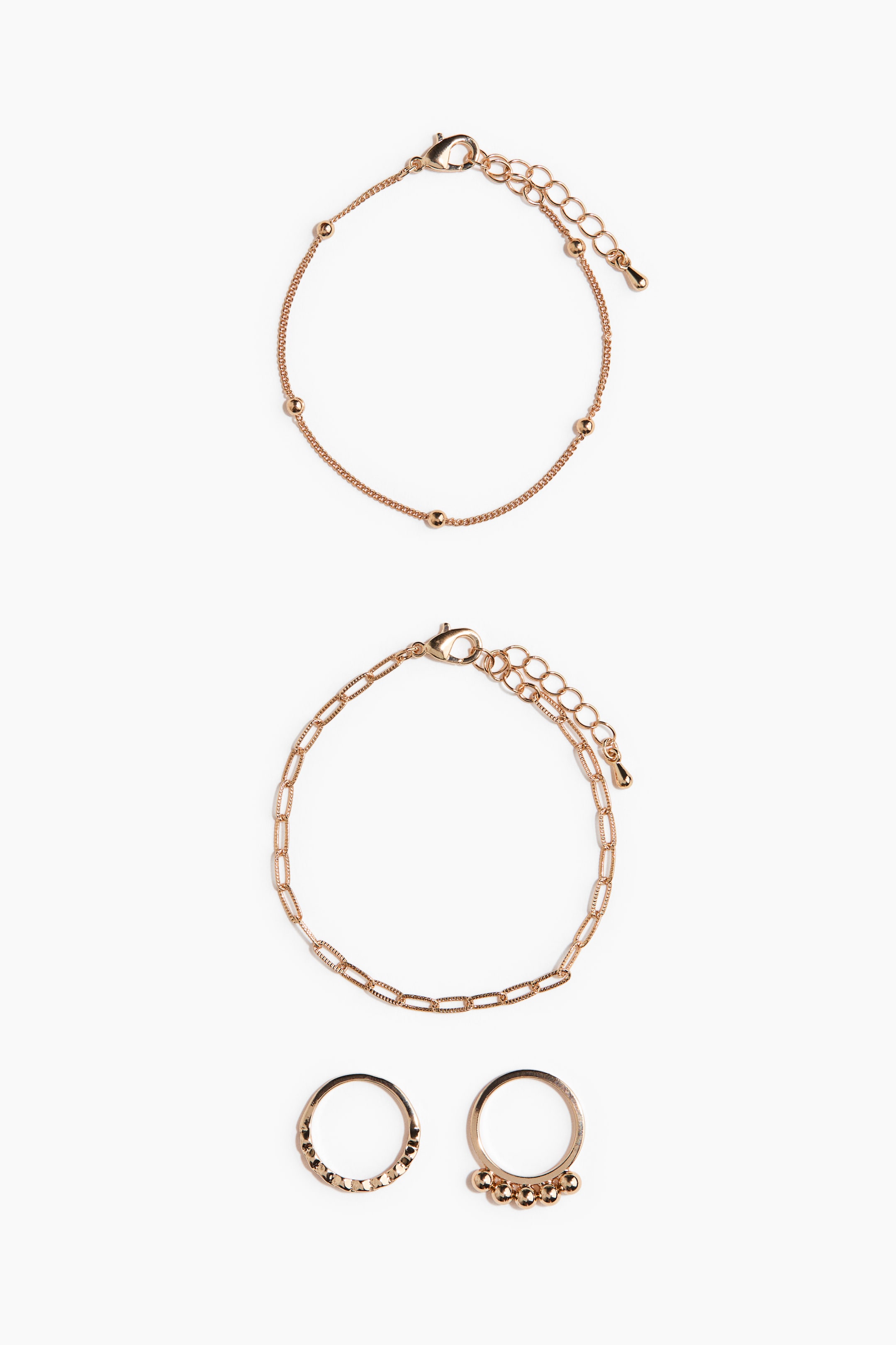 Visualizza immagine più grande: Questo set di gioielli color oro rosa presenta due bracciali e due anelli disposti verticalmente. Il bracciale in alto mostra una delicata catena con piccole perline distanziate, mentre quello al centro presenta un design a catena paperclip. Sotto sono posizionati due anelli coordinati, uno con una fascia testurizzata e sfaccettata e l’altro con cinque piccoli charm pendenti a forma di perla.
