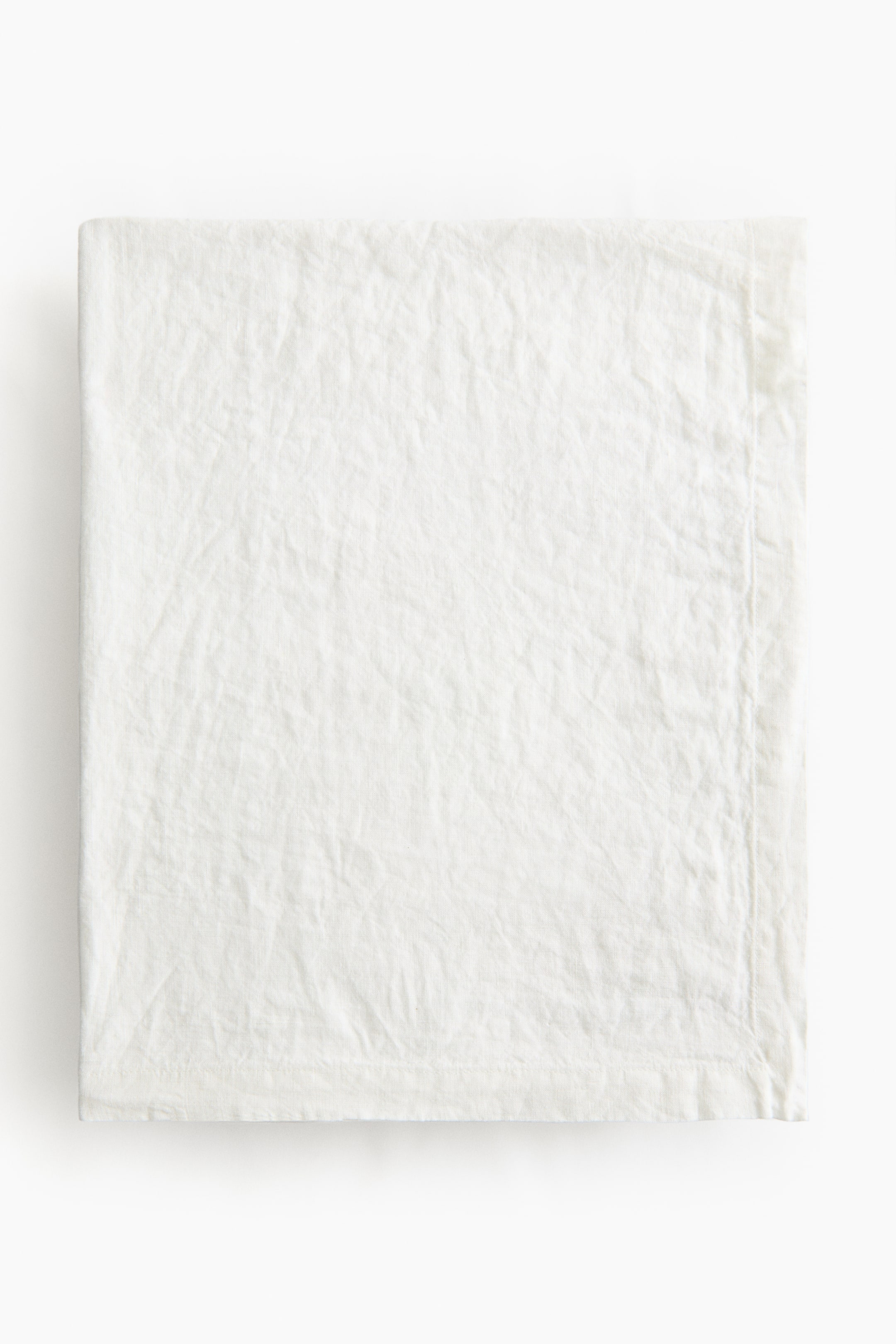 Agrandir l'image: Une nappe de couleur crème est étendue à plat, mettant en valeur un tissage en lin texturé et un ourlet replié le long de ses bords.
