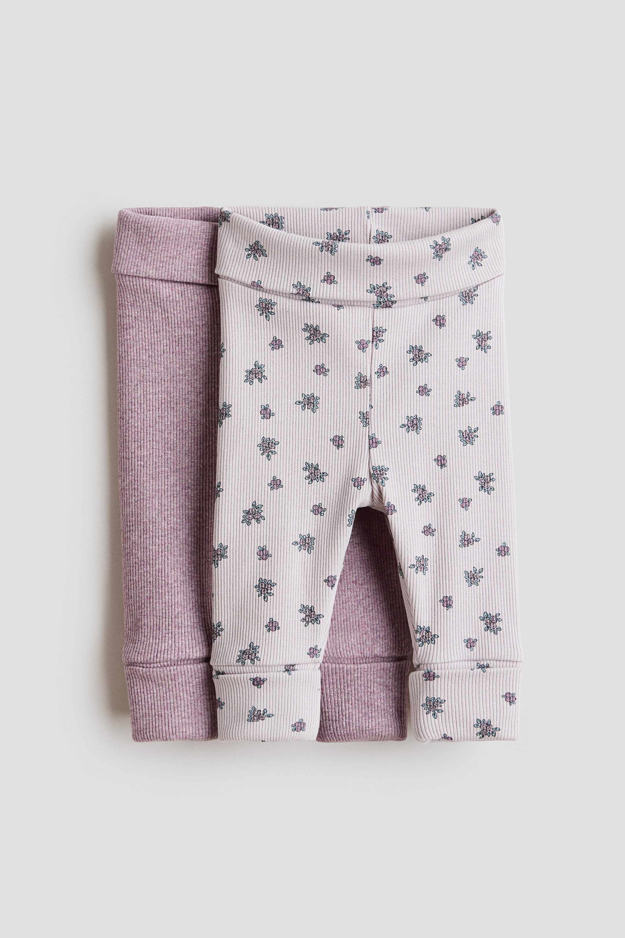 查看大圖: 兩對 H&M Adorables 羅紋針織打底褲,設有寬大的翻折腰部面板和加長的袖口,目前在下擺處折起。前面的一對展示了淺粉紅色背景配花卉圖案,而後面的一對則是純紫色。