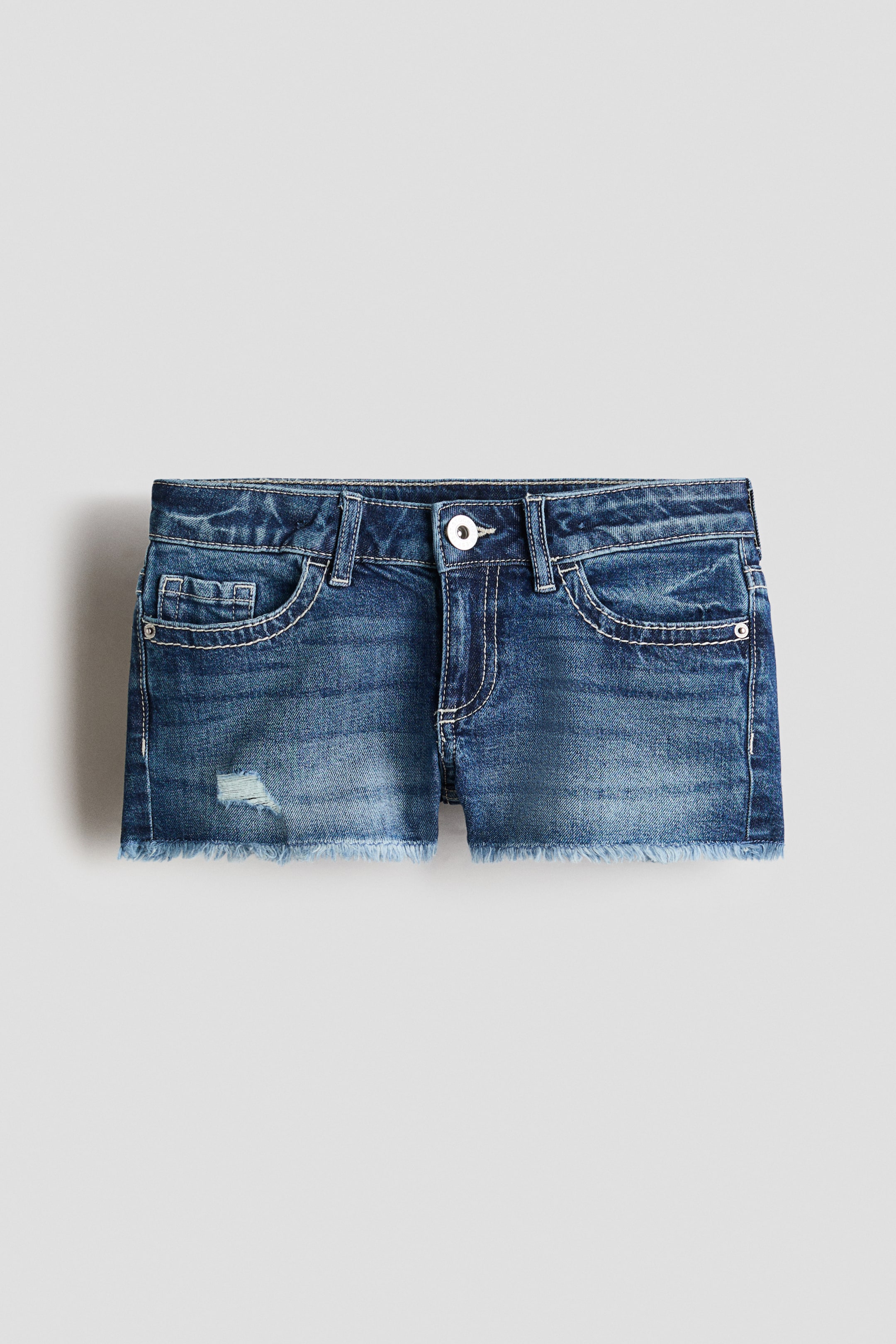 View larger image: Denim shorts are showcased from the front, featuring a faded blue wash with a visible waistband, belt loops, and a single button fastening above a zip fly. They display front pockets with contrasting stitching, a distressed detail on the left leg, and a raw, frayed hem.