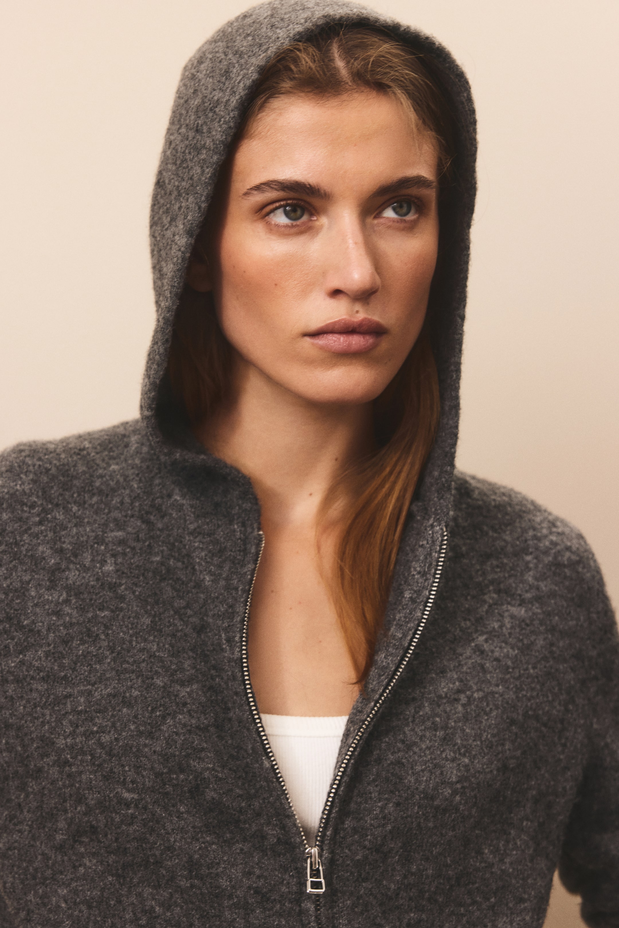 View larger image: A dark gray, soft-knit zip-up hoodie is shown from the front with the hood pulled up. The partially unzipped front reveals a white ribbed top layered underneath the textured wool-blend fabric.