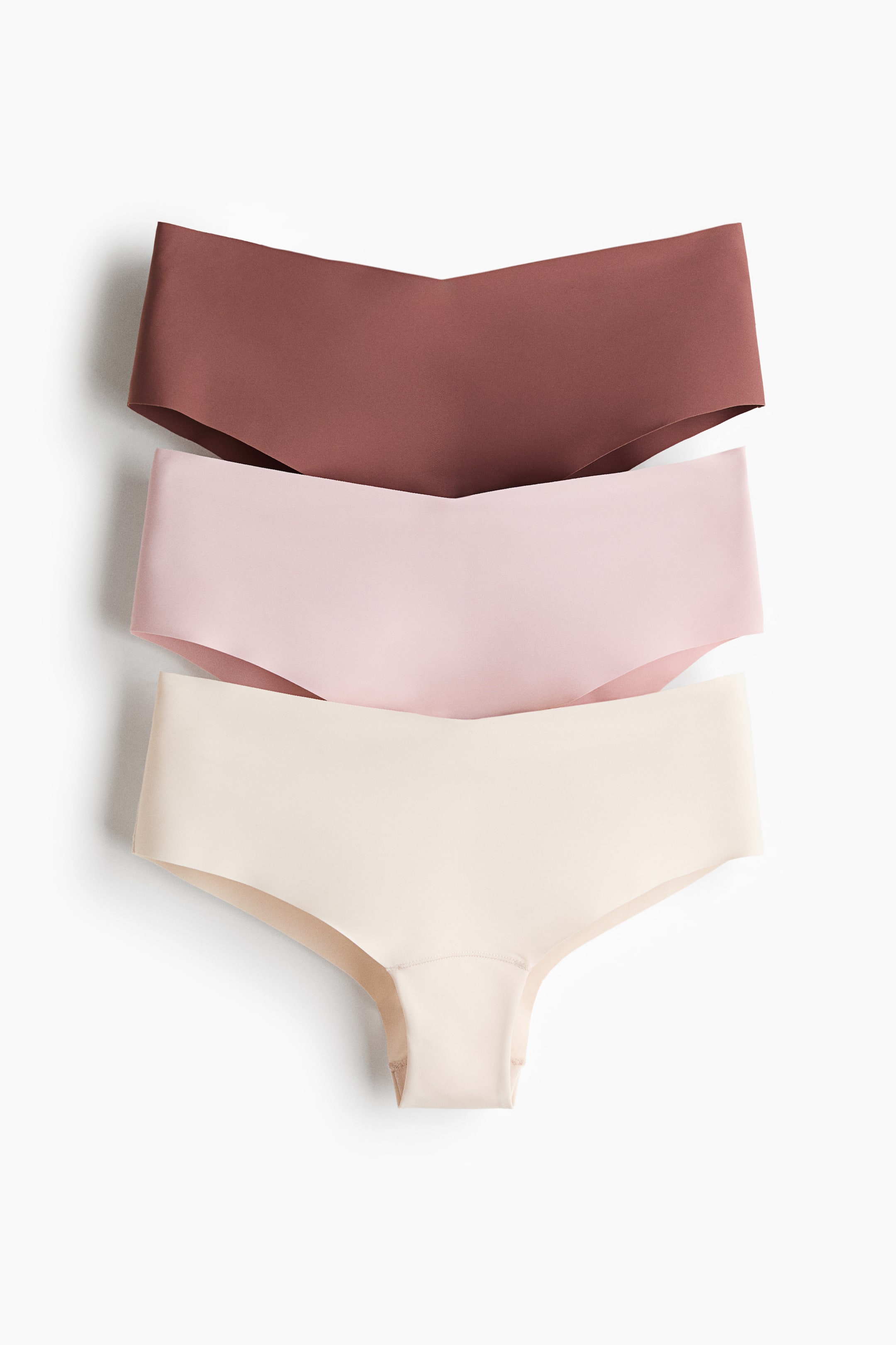 View larger image: Three pairs of seamless knickers are stacked, showcasing their front view. The top pair is a reddish-brown, the middle is light pink, and the bottom is beige, all featuring smooth, unstitched edges.