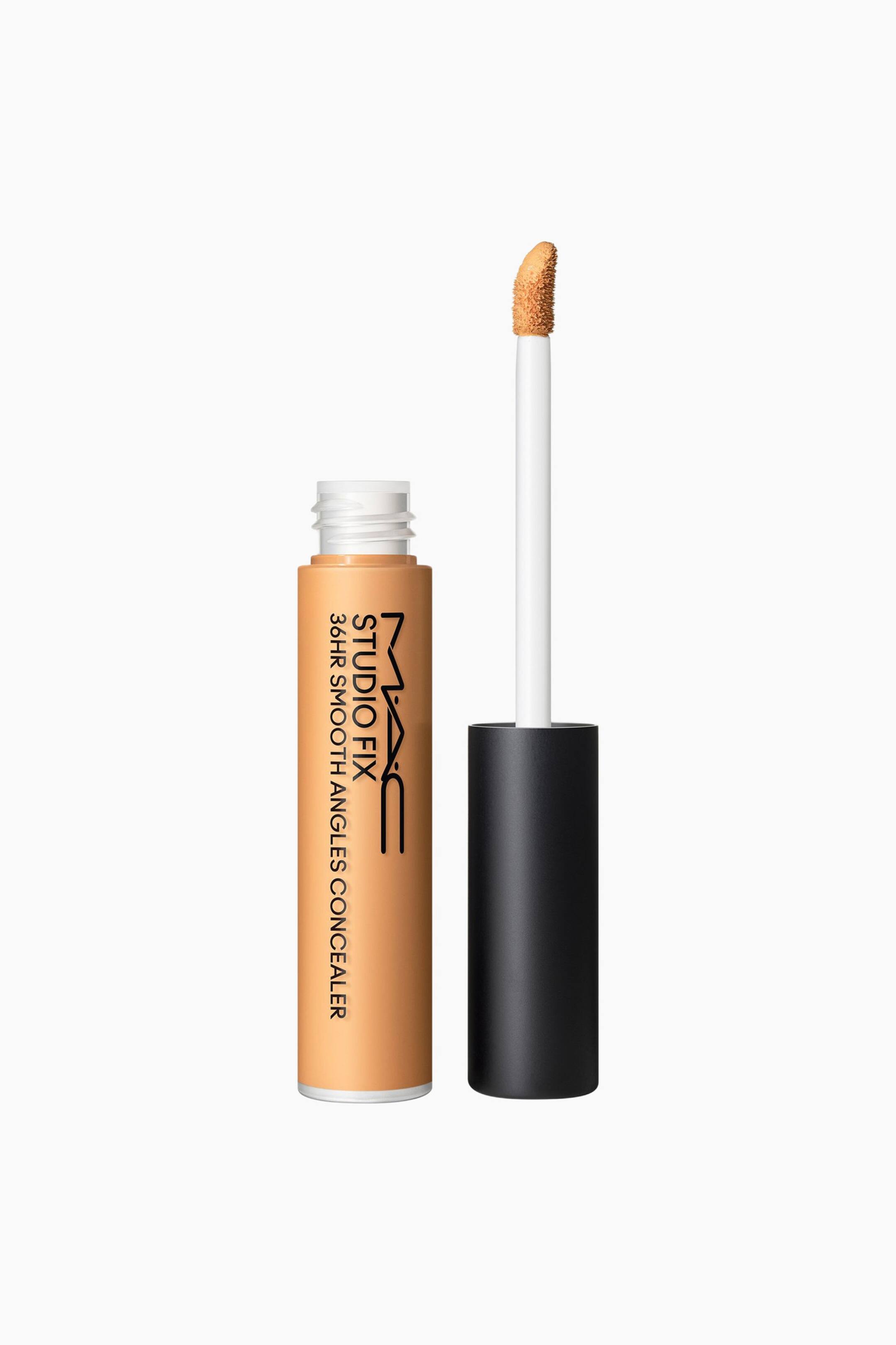 Se større billede: Et tan MAC Studio Fix 36HR Smooth Angles Concealer-rør står oprejst, og viser sin sorte produkttekst samt en åben top med synlige hvide skruegevind. Dets applikator, der har en hvid stav med en tan padleformet spids, står oprejst ved siden af røret, fastgjort til et sort håndtag.
