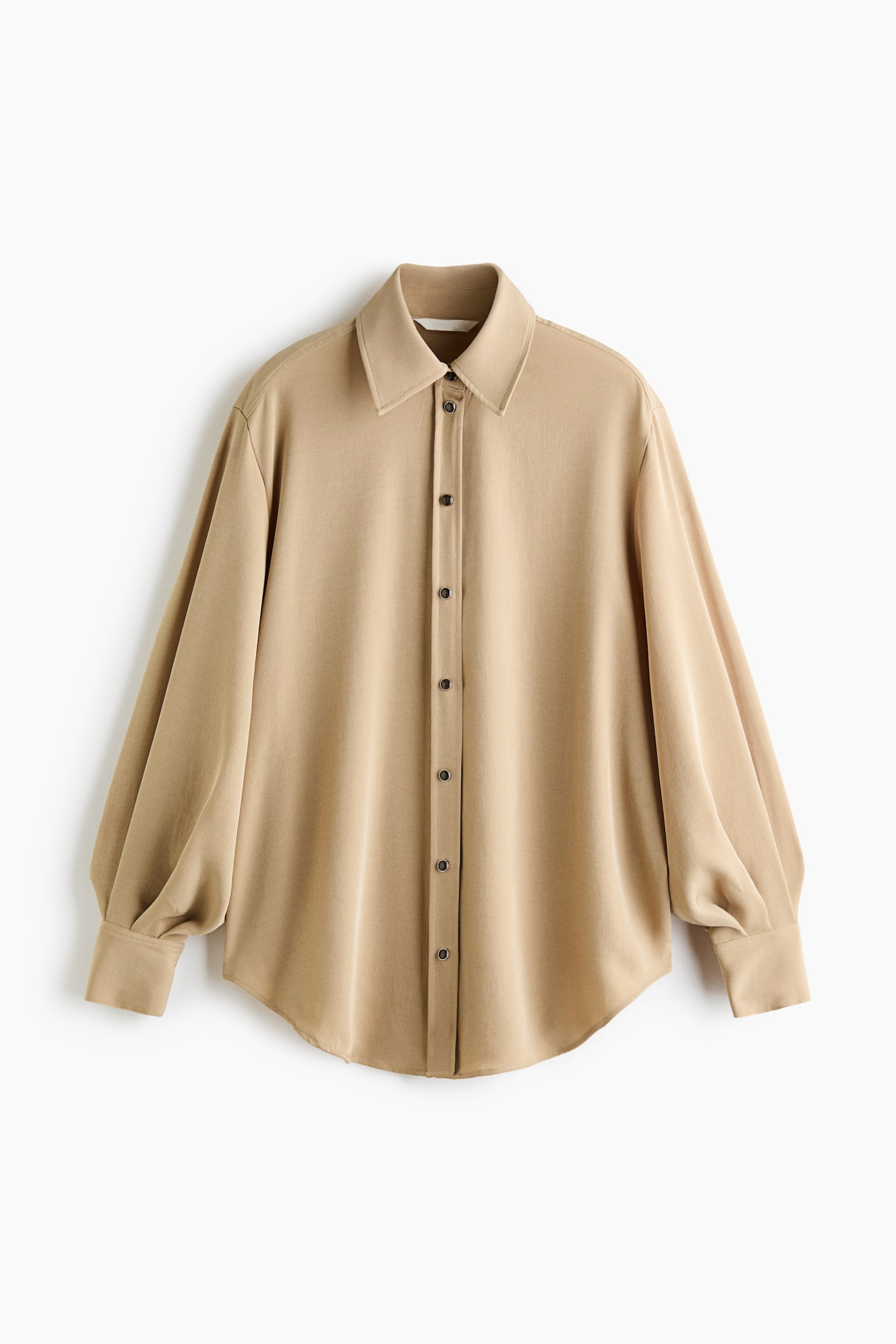 En oversized beige skjorte i vevd stoff vises forfra, med spiss krage, senkede skuldre og en frontslÃ¥ med mÃ¸rke marmorerte knapper. Skjorten er designet med lange ballongermer som avsluttes med brede mansjetter og en mykt avrundet kant nederst.