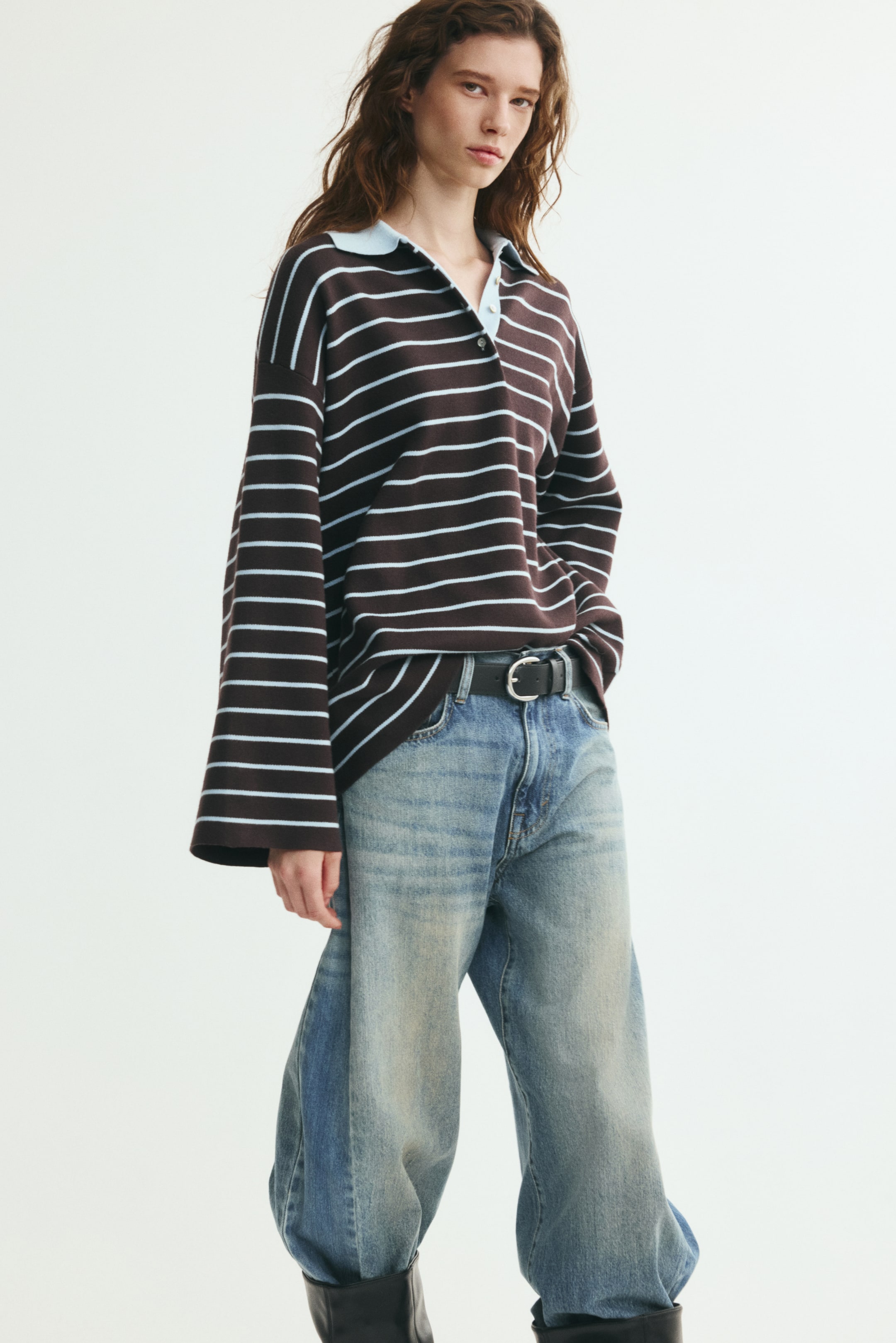 Visa större bild: En oversized pikétröja med horisontella ränder i brunt och ljusblått, en kontrasterande ljusblå krage och långa vida ärmar bärs av modellen. Tröjan är delvis instoppad i vida blå jeans som stylats med ett svart bälte.