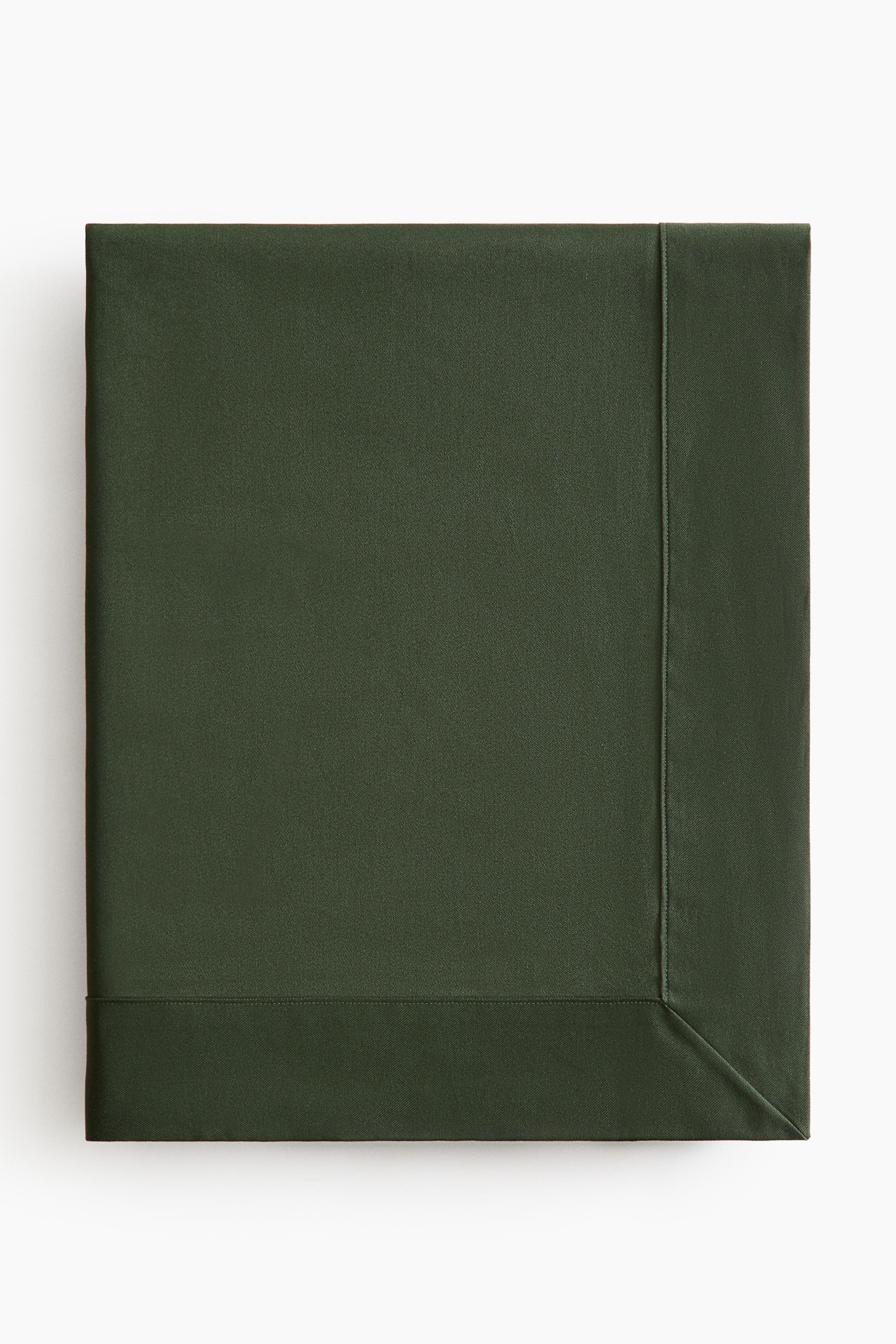 View larger image: A dark green tablecloth is shown folded flat, facing front, showcasing a wide stitched hem and a diagonal mitred corner. The solid-coloured cotton fabric features a smooth, matte texture with clean stitched borders.
