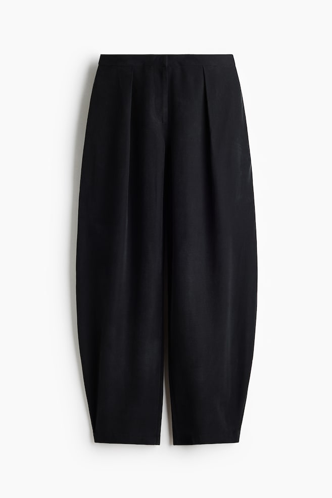 Black pants are shown from the front, featuring a flat waistband and two prominent front pleats. Their wide legs are forming a rounded, voluminous silhouette, ending with a straight, cropped hem. - 1