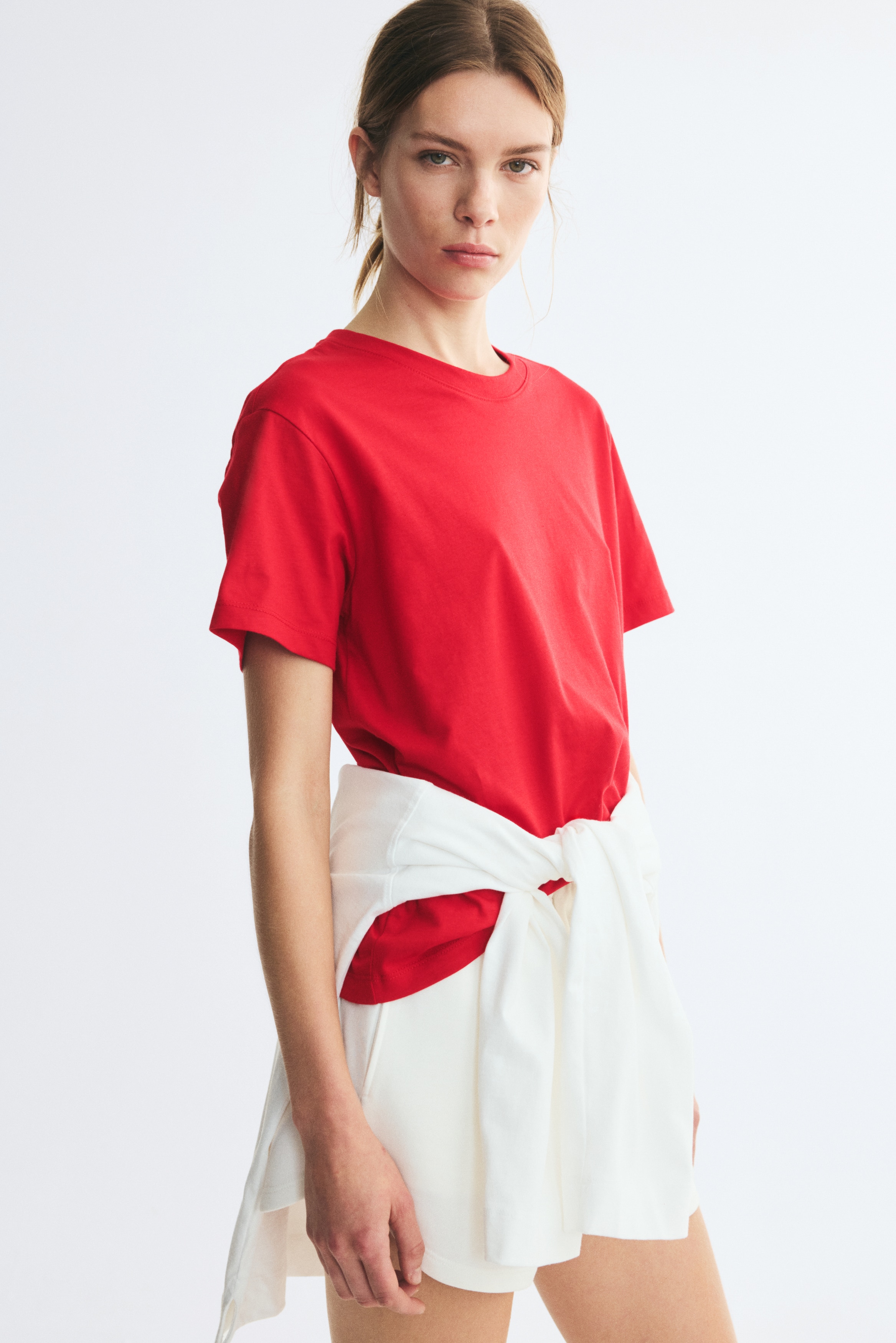 A straight-cut red t-shirt in soft cotton jersey is facing as front, showcasing a relaxed silhouette. The t-shirt is featuring a round, rib-trimmed neckline and short sleeves with gently dropped shoulders.