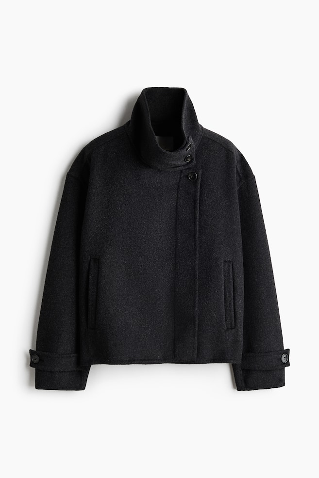 Een donkergrijs, oversized gevilte jasje is van voren afgebeeld en toont een hoge opstaande kraag met een asymmetrische knoopsluiting, verlaagde schouders, steekzakken in de zijnaad en manchetten met knoopbandje. - 1