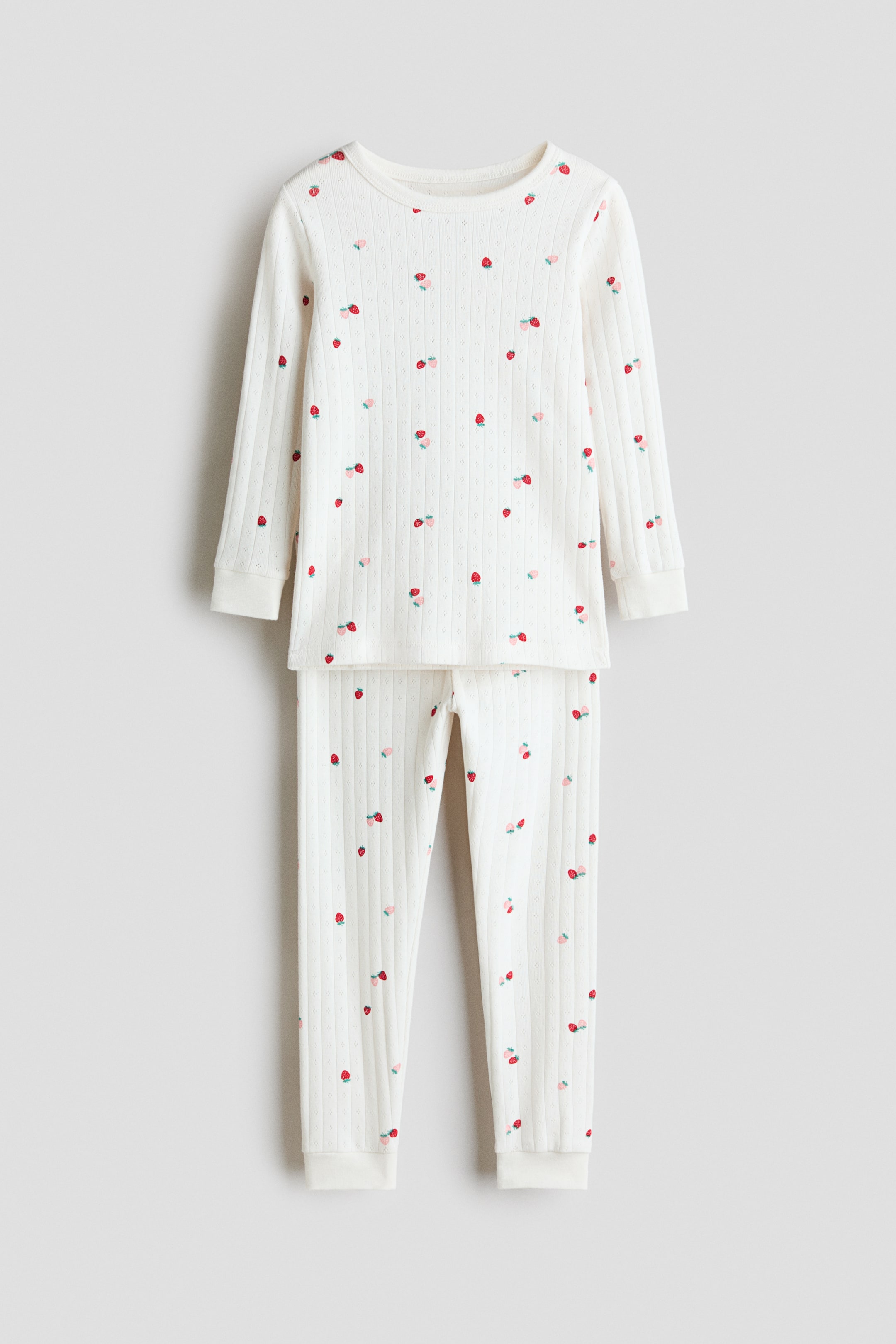 Voir une image plus grande: Un ensemble de pyjama deux pièces de couleur crème présente une texture côtelée et un imprimé de fraises éparses, présenté de face. Le haut à manches longues affiche un col rond et des poignets côtelés, tandis que le pantalon assorti présente des bords-côtes aux chevilles.