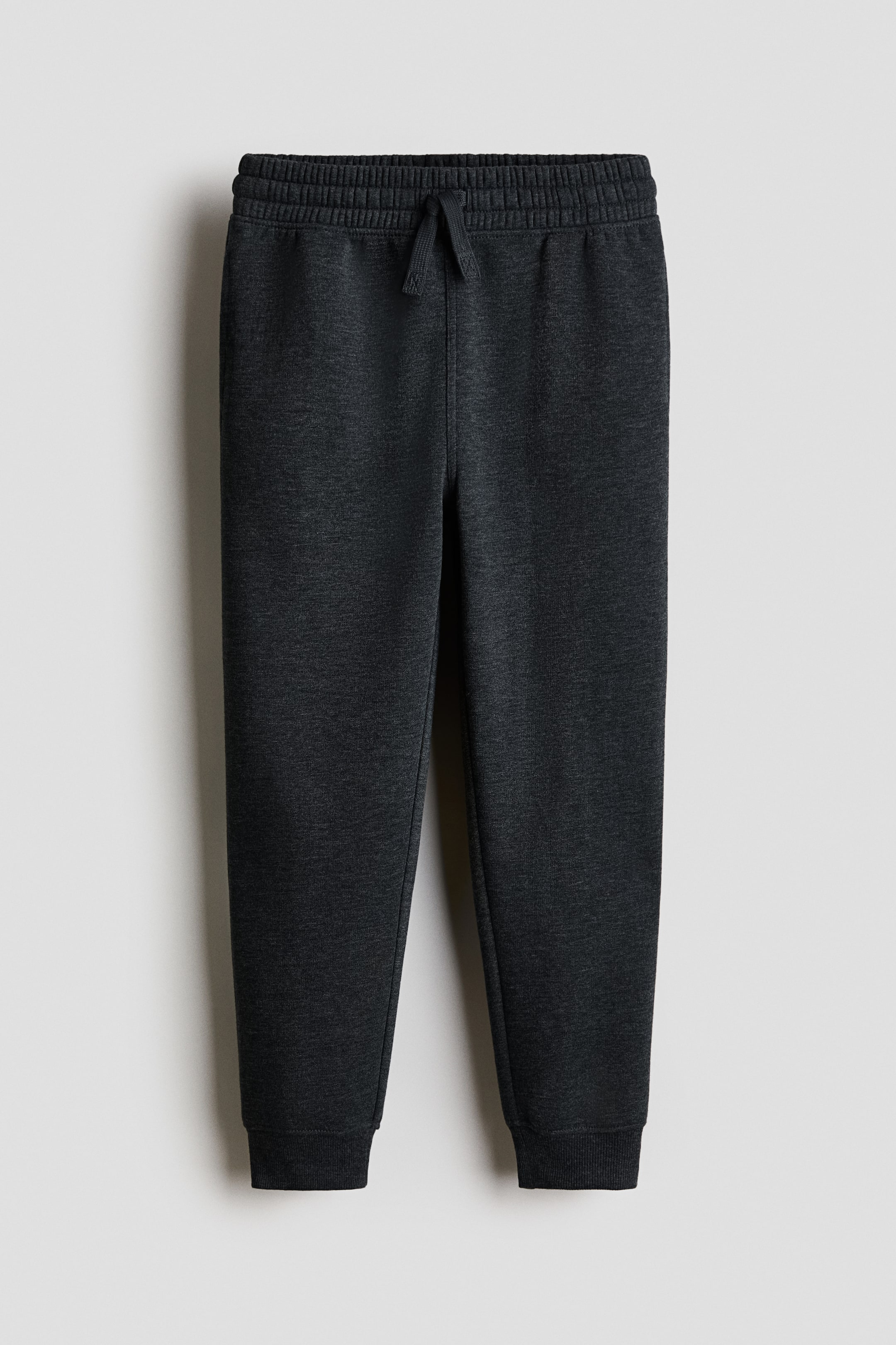 Nagyobb kép megtekintése: A sötétszürke joggerek elölről láthatók, melírozott melegítőanyagból készültek. Gumis, húzózsinóros derékrésszel (a zsinór megkötve), oldalzsebekkel és szűkített szárakkal rendelkeznek, amelyek bordás szegélyben végződnek.