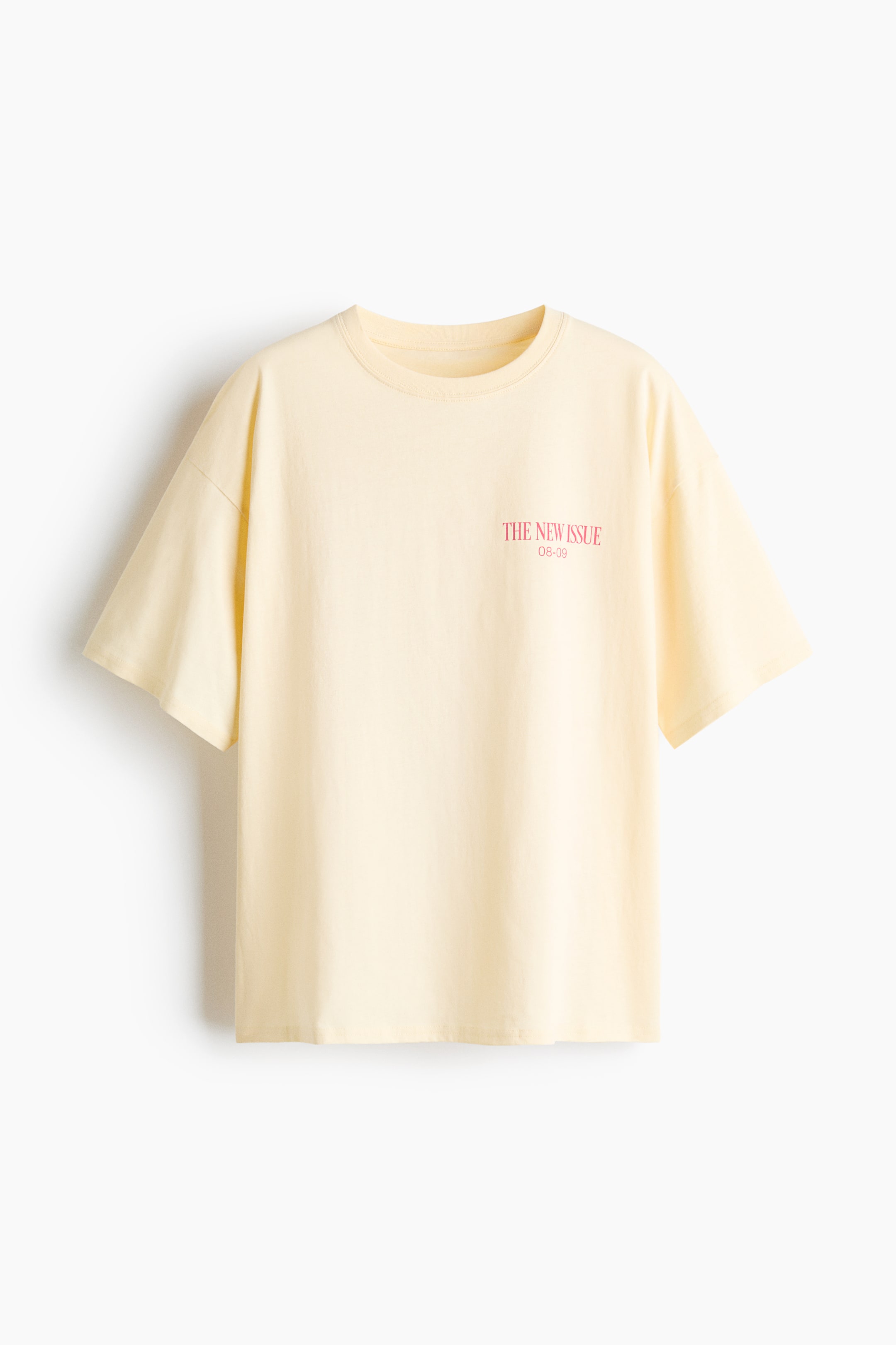 拡大画像を表示: コットンジャージー製のライトイエローのオーバーサイズTシャツが前面を見せており、胸部には「THE NEW ISSUE 08-09」と書かれた小さなピンクのテキストプリントが特徴です。ネックラインにはリブトリムが施され、ドロップショルダーとストレートカットの裾がデザインされています。