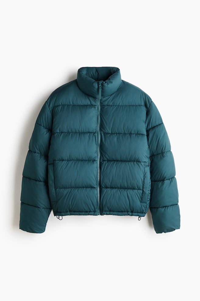 A teal puffer jacket is hanging facing forward, presenting a high stand collar, horizontal quilted panels, and a full-length front zipper. It is featuring welt side pockets and small drawcord loops peeking out at the bottom hem. - 1
