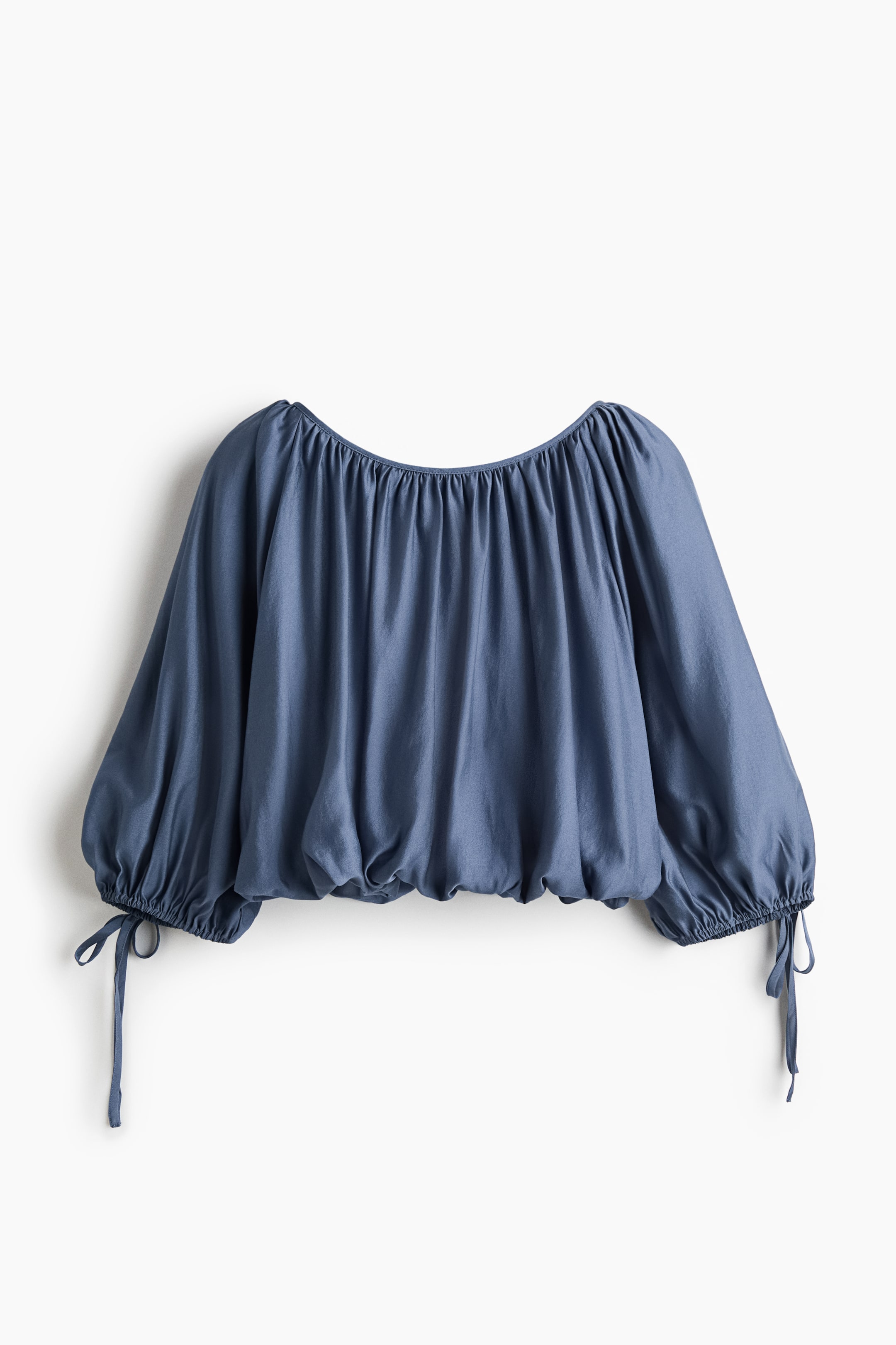 Ver imagen más grande: Un top azul con un escote amplio y fruncido, mangas largas y voluminosas que se recogen en los puños con lazos decorativos, y un dobladillo inferior fruncido que forma una silueta tipo blusón.