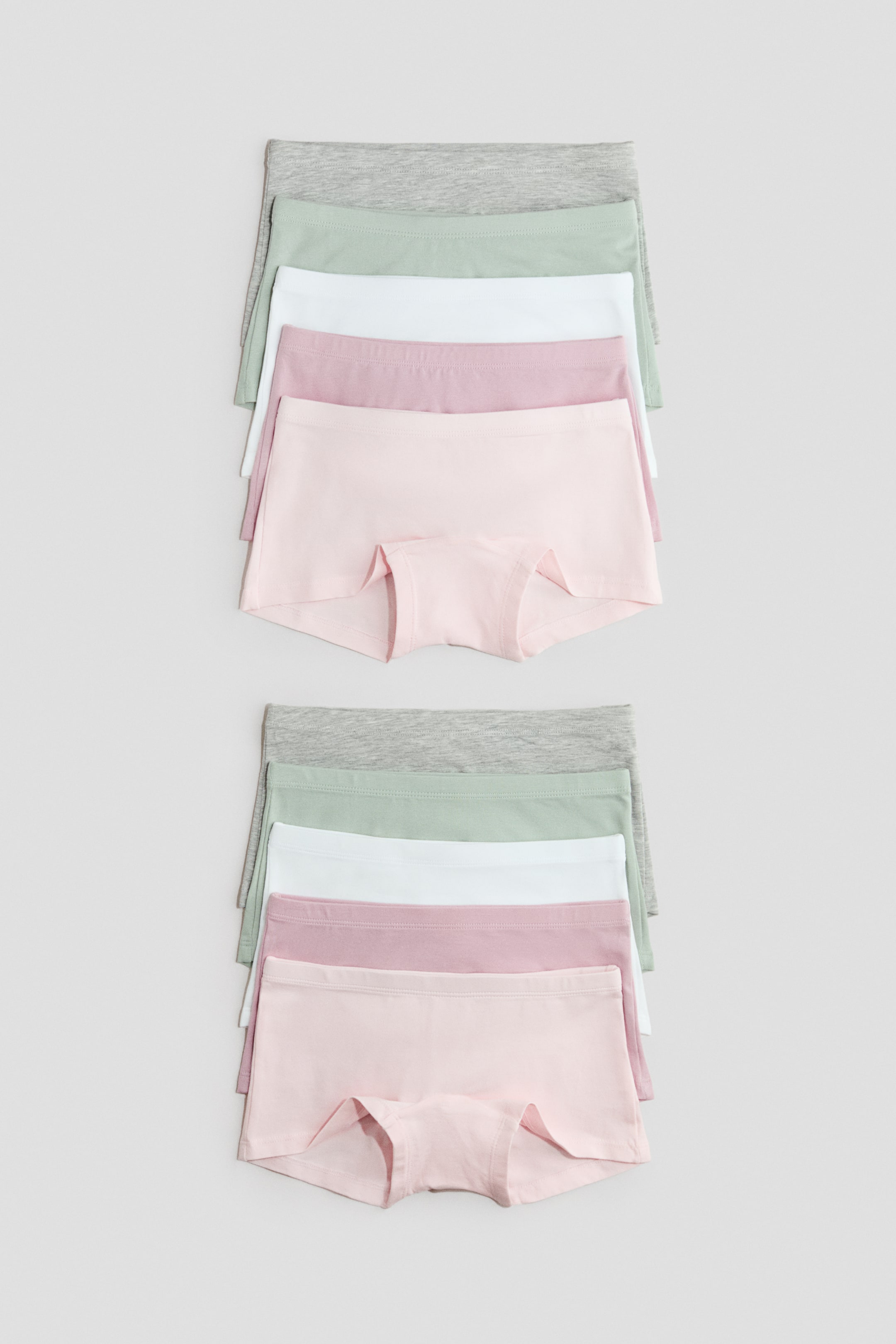View larger image: Boy short underwear are showcased in two identical stacks of five pairs, neatly folded to reveal a flat waistband and full-coverage design from the front. The stacks display colours including light grey, light green, white, dusty rose, and light pink.