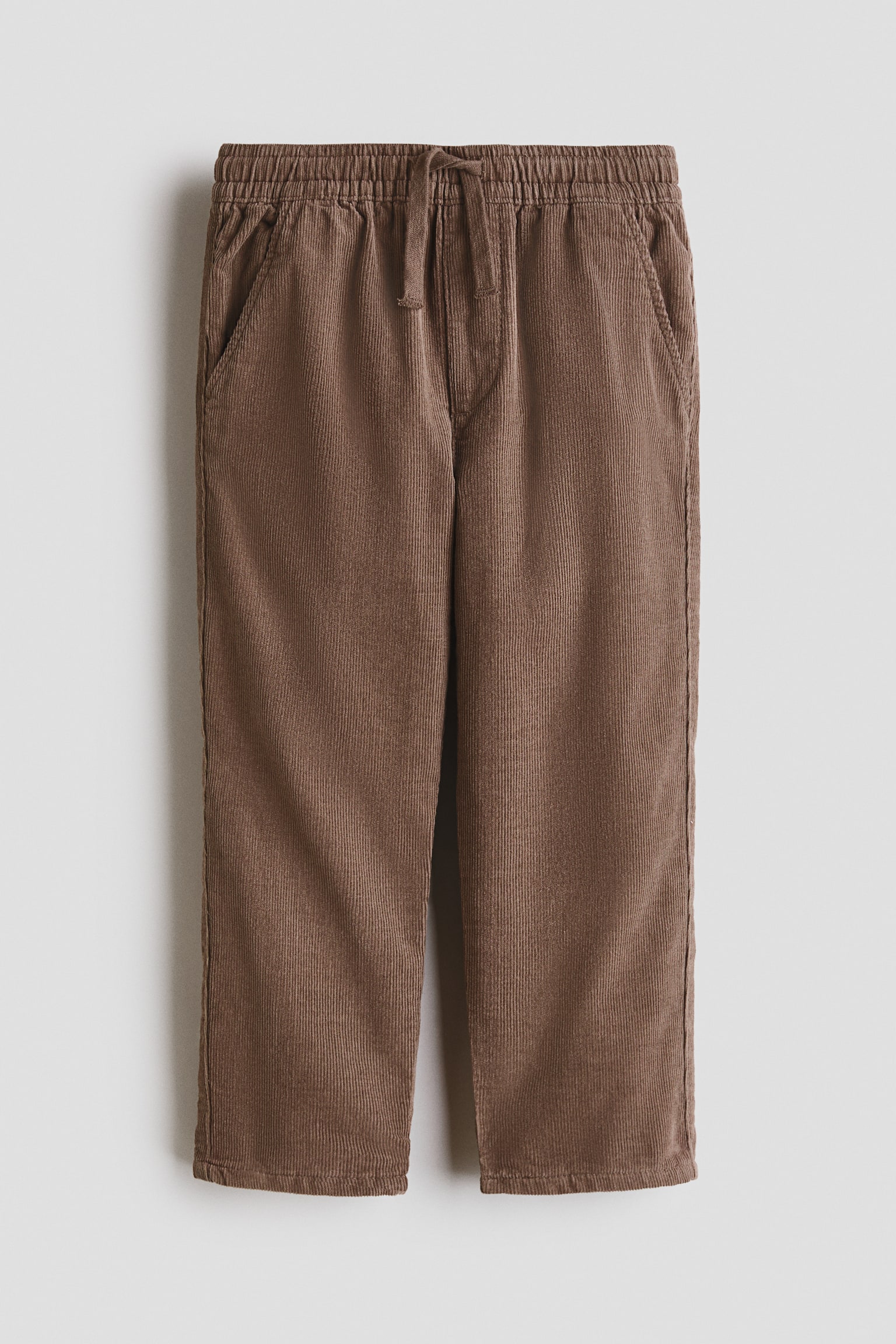 Pantalones de pana marrón suave presentados de frente, con cintura elástica con cordón ajustable, bragueta simulada y bolsillos laterales inclinados, de corte holgado en la cadera y el muslo, y pernera que se estrecha suavemente hacia el bajo. - 1
