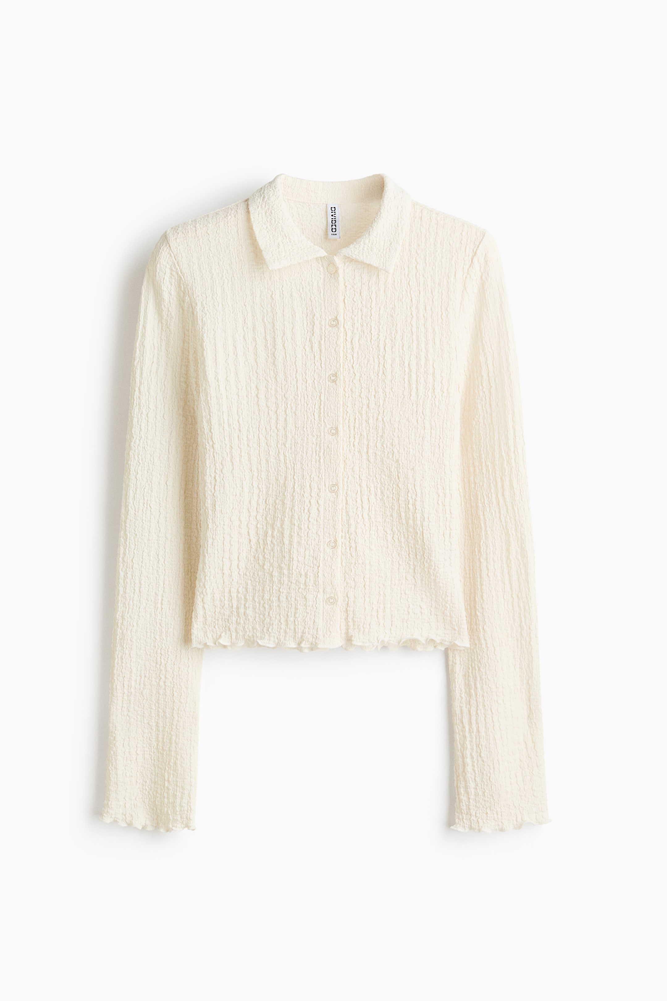 View larger image: A cream-colored, front-facing collared top is featuring a crinkled texture throughout, a button-front placket, long sleeves, and lettuce-edge cuffs and hem.