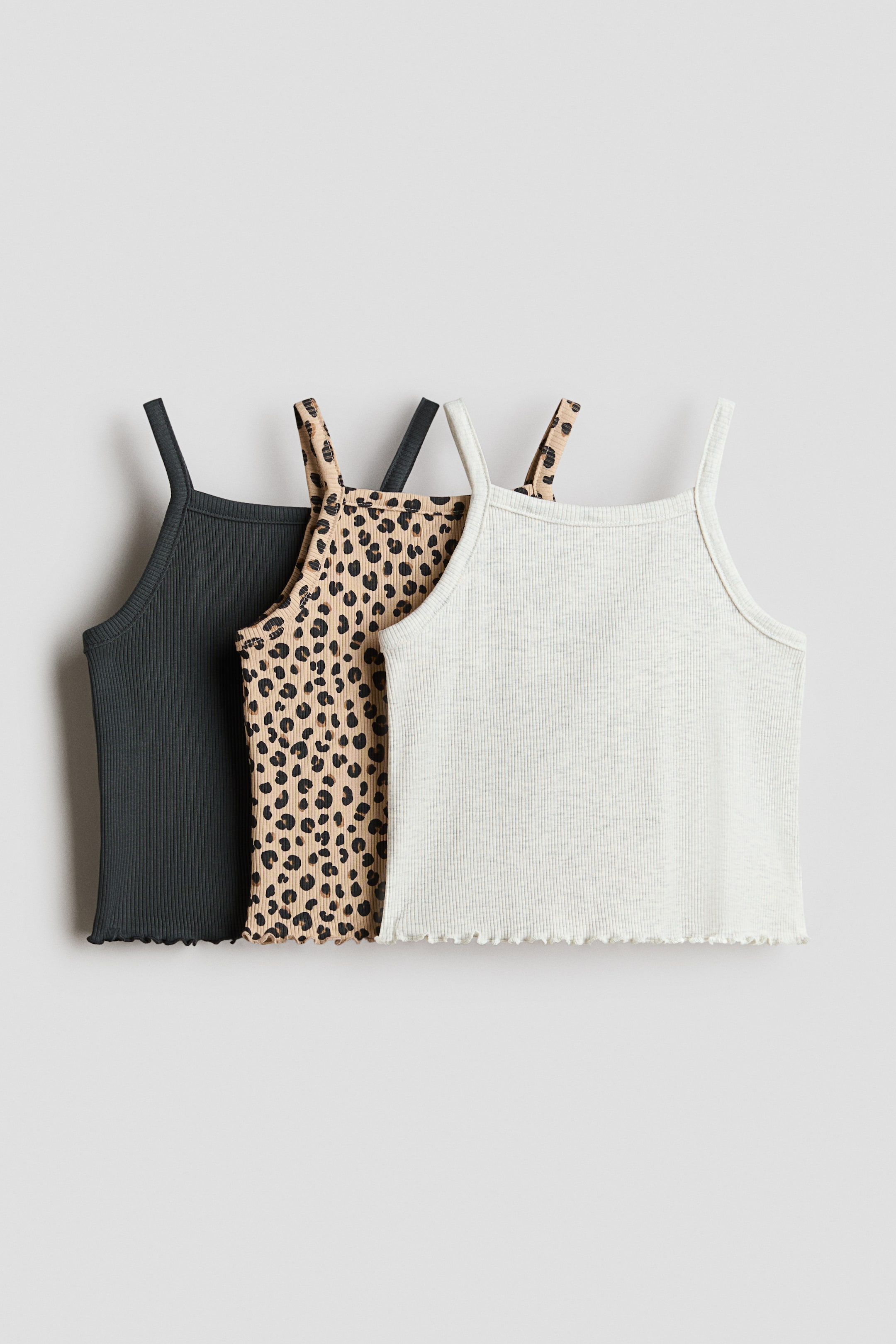 View larger image: Three camisole tops are showcased with their fronts visible, layered slightly one behind the other. Each top boasts thin spaghetti straps, a square neckline, ribbed knit fabric, and a wavy lettuce-edge hem, available in dark grey, beige with a black leopard print, and light grey.