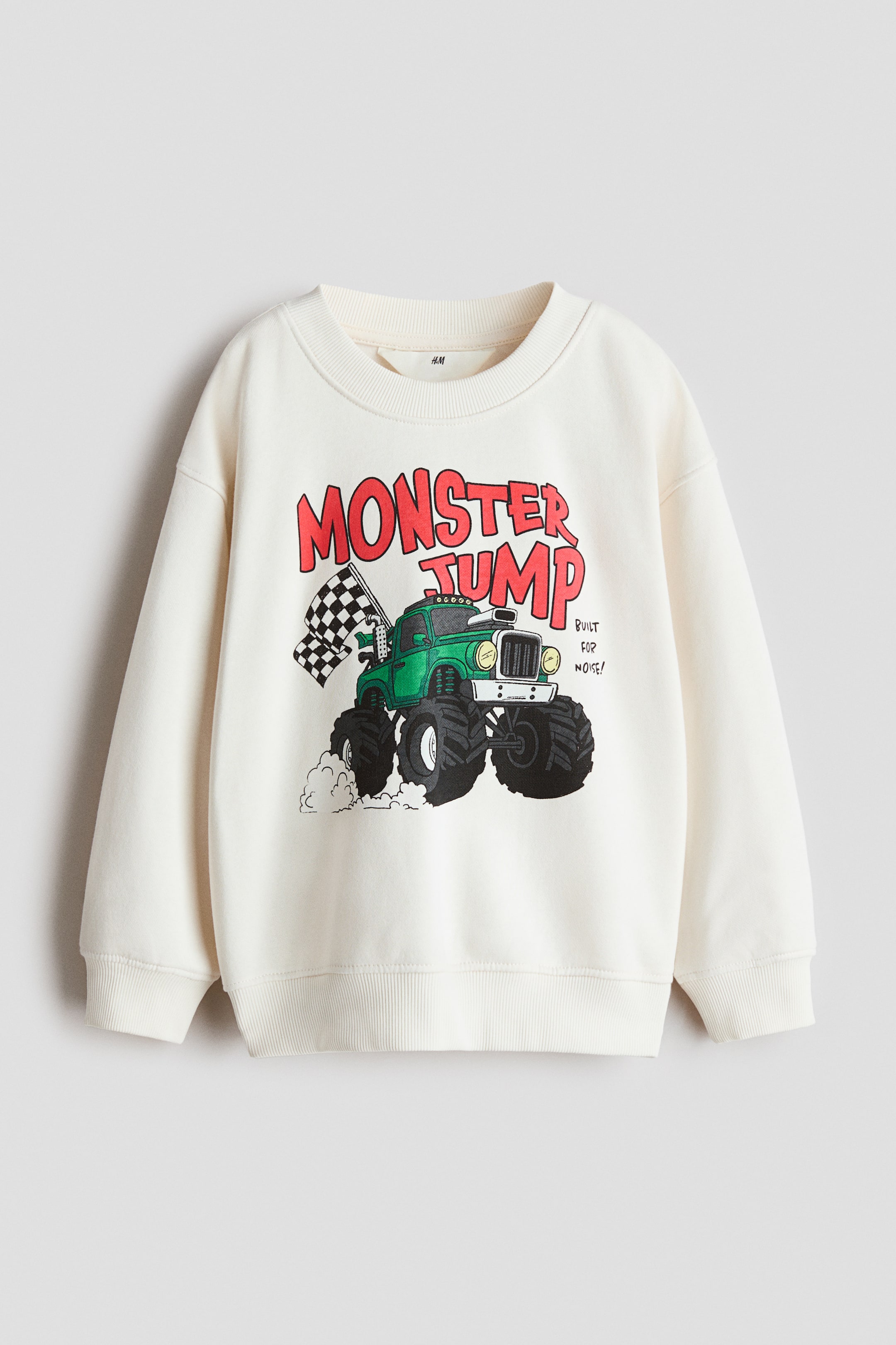 View larger image: An off-white, loose-fit sweatshirt is shown from the front, featuring a graphic print of a green monster truck with a checkered flag and red text reading "MONSTER JUMP." The design includes a ribbed round neckline, dropped shoulders, and ribbed trim at the cuffs and hem.