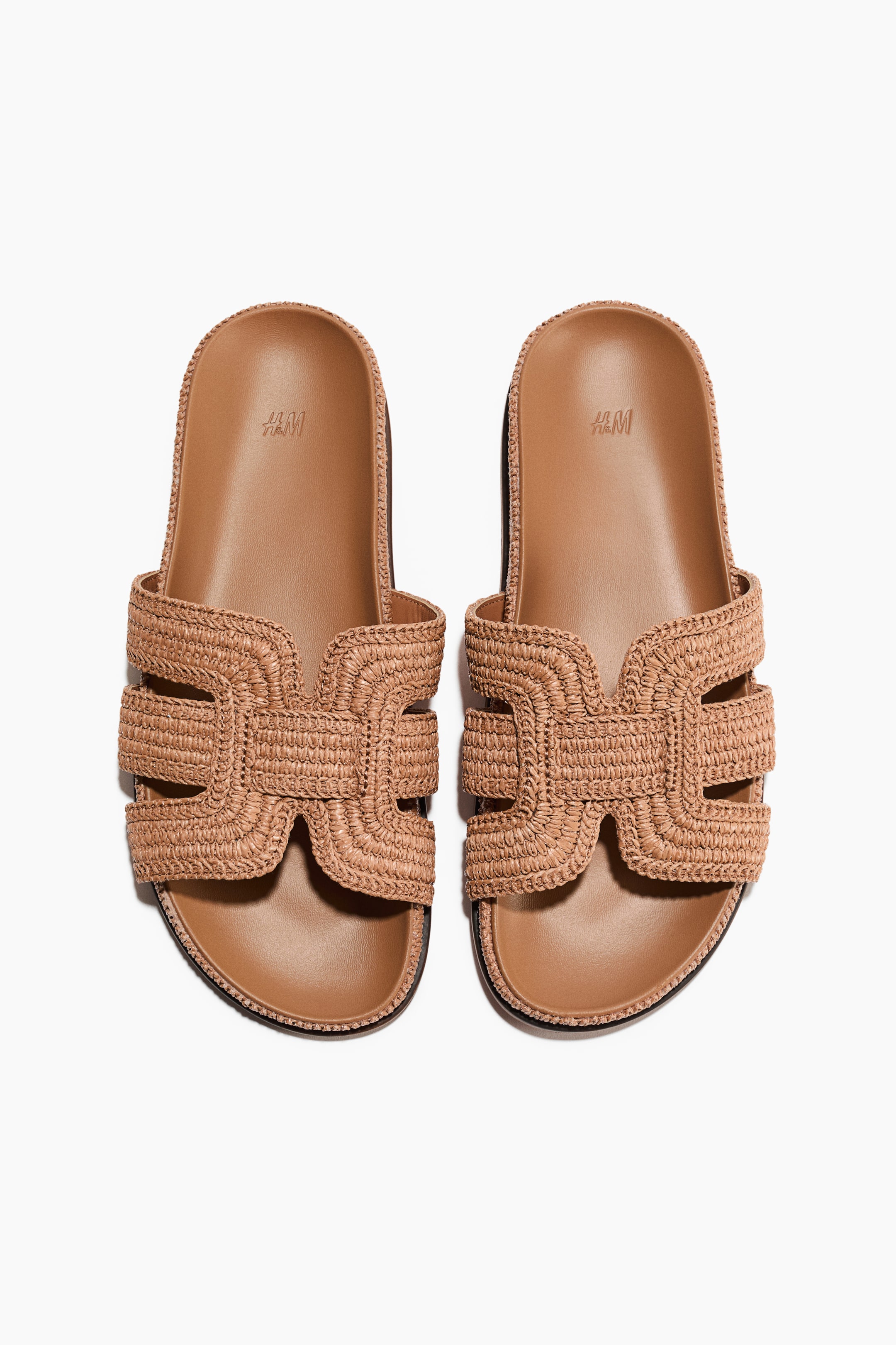 View larger image: A pair of sandals featuring wide, H-shaped foot straps in braided straw, tan moulded insoles, and oblique toe shapes, presented facing front.