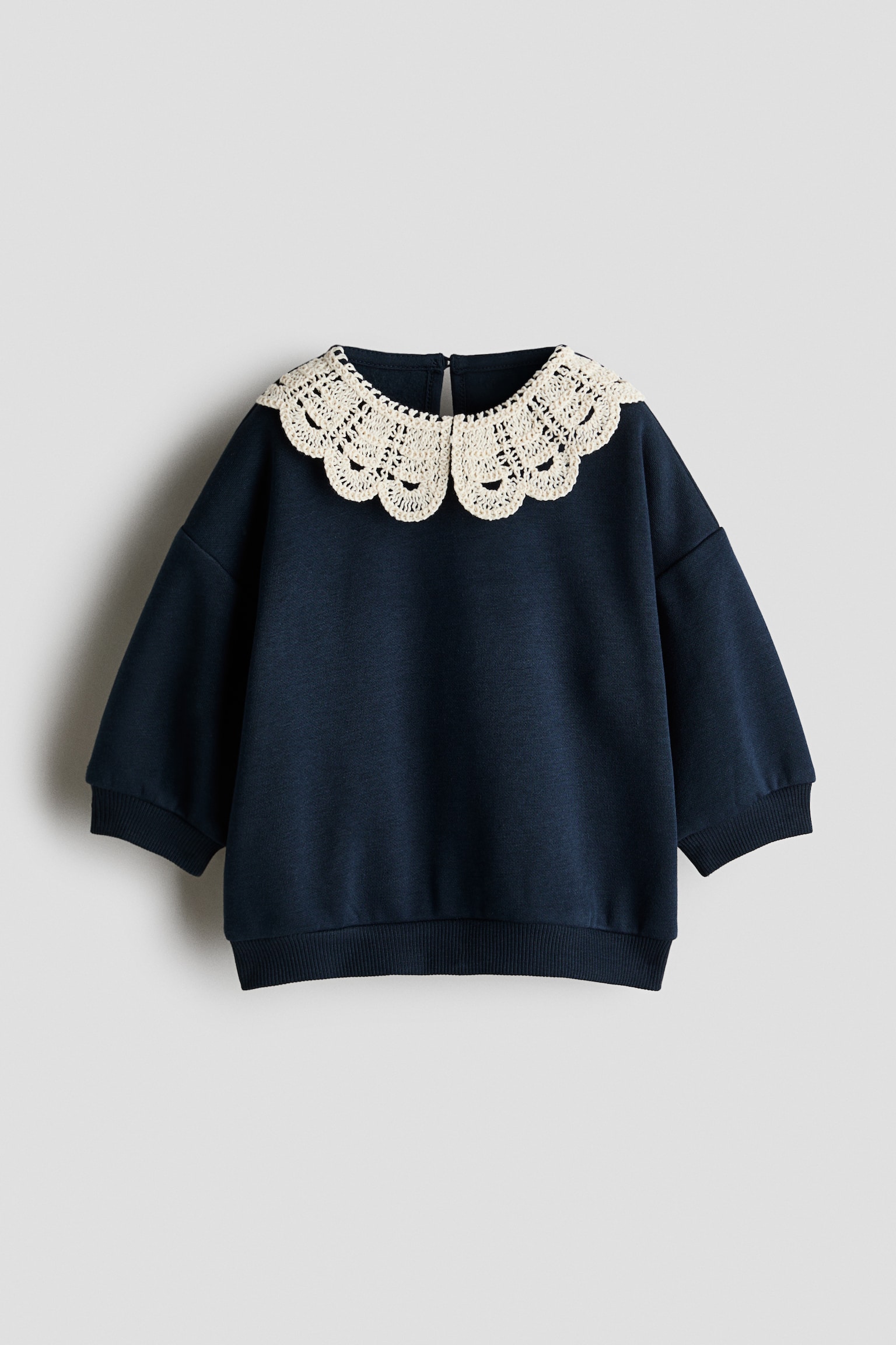 Má»t chiáº¿c Ã¡o sweatshirt mÃ u xanh navy ÄÆ°á»£c chá»¥p tá»« phÃ­a trÆ°á»c, ná»i báº­t vá»i pháº§n cá» Peter Pan cá»¡ lá»n mÃ u kem, Äan mÃ³c, cÃ³ chi tiáº¿t viá»n lÆ°á»£n sÃ³ng. Thiáº¿t káº¿ Ã¡o cÃ³ vai trá», tay dÃ i vá»i bo tay gÃ¢n vÃ  gáº¥u Ã¡o gÃ¢n Äá»ng bá».
