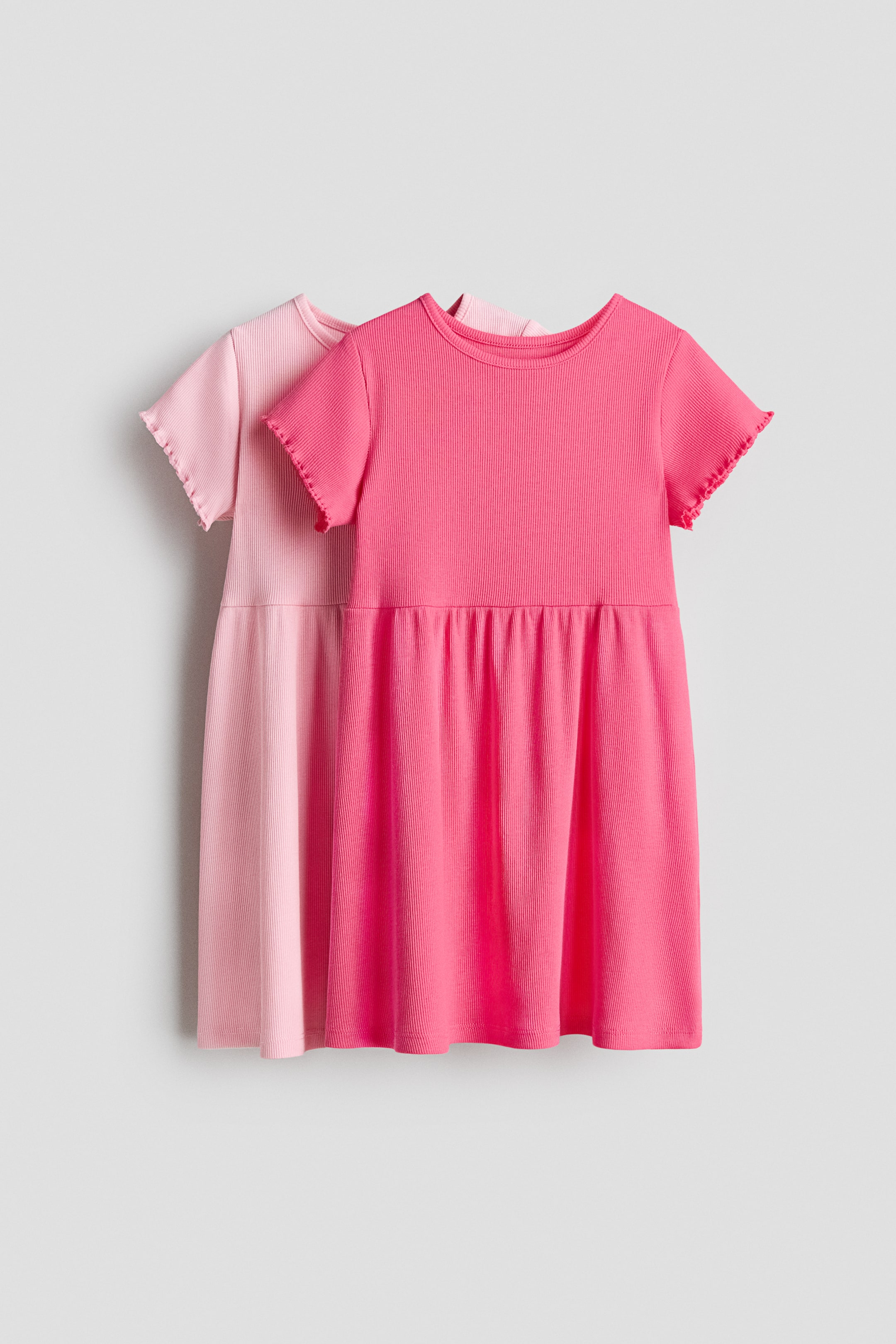 Visualizza immagine più grande: Due abiti a maglia a coste sono presentati frontalmente. L'abito fucsia è sovrapposto a un abito rosa chiaro, e entrambi presentano uno scollo rotondo, maniche corte con bordi arricciati e una gonna arricciata.