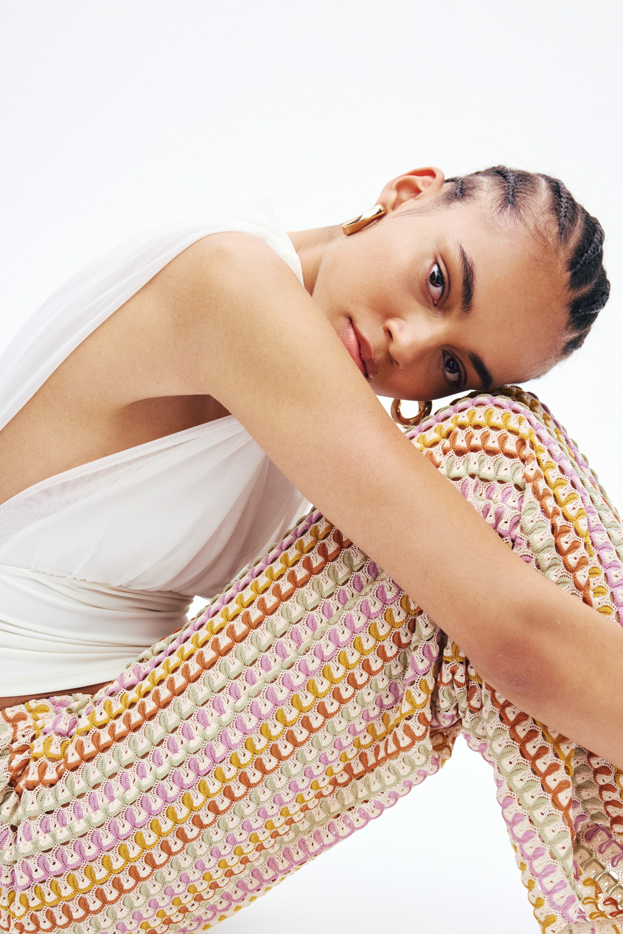 View larger image: Trousers are boasting a multi-coloured, intricate scallop pattern in shades of pink, orange, yellow, and green, resembling a textured knit fabric. They are draping around a bent leg, highlighting the detailed pattern.