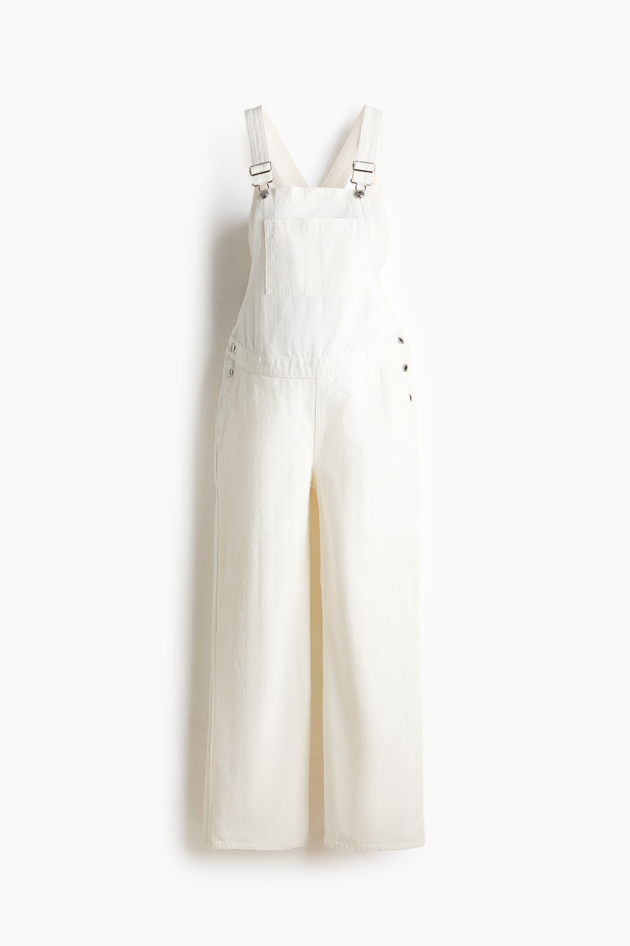 View larger image: The white denim overalls are shown from the front, featuring adjustable shoulder straps with metal buckles and a patch chest pocket. They also display diagonal side pockets, buttons on both sides of the waist, and straight legs.
