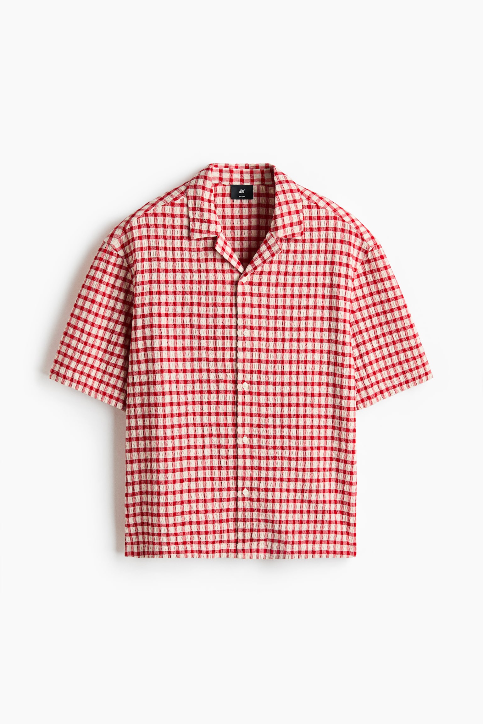"A short-sleeved shirt showcases a red and off-white gingham check pattern with a crinkled texture, featuring a revere collar and a full button-front closure with light-colored buttons."