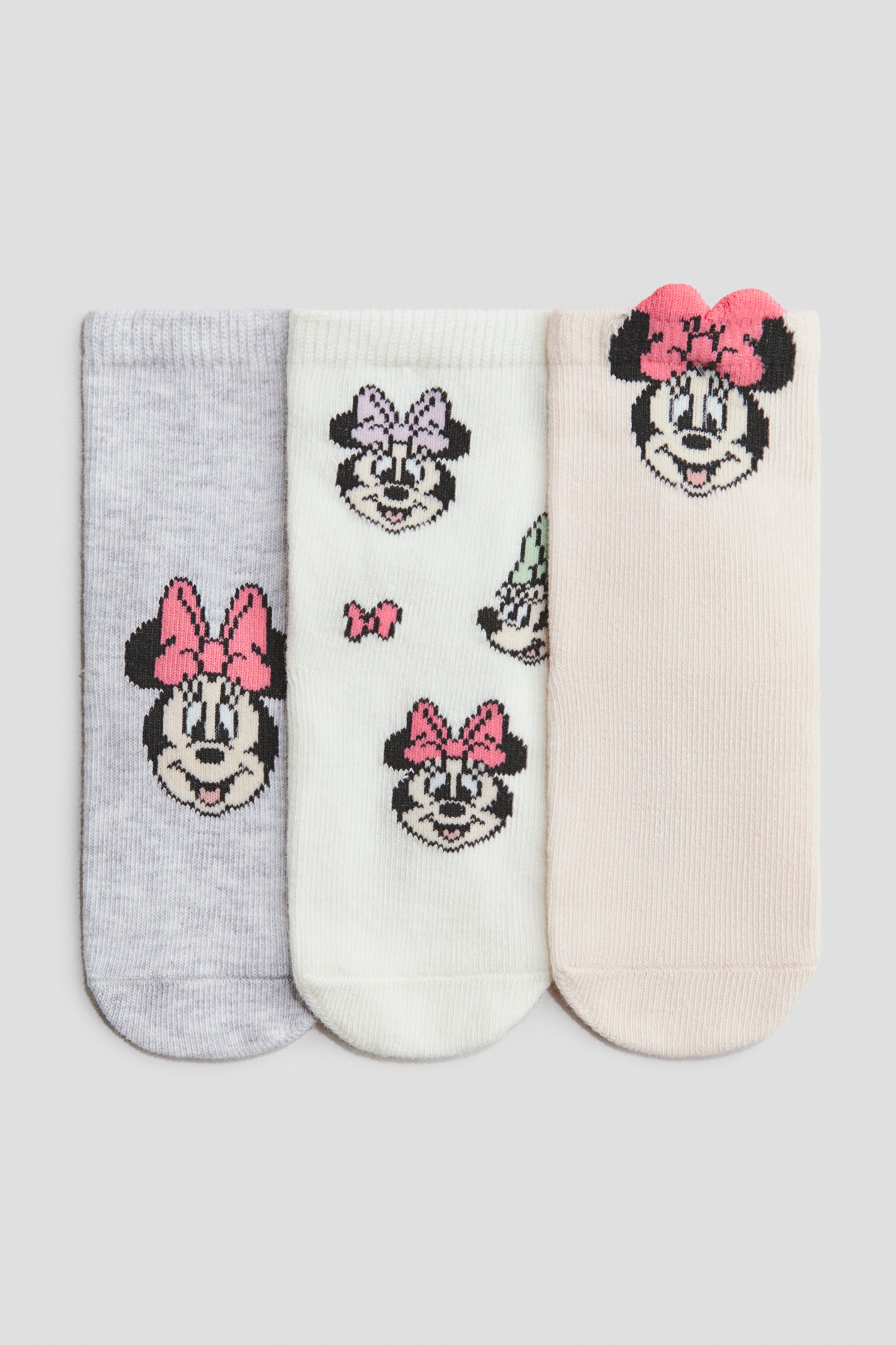 View larger image: Three fine-knit socks are lying flat, facing FRONT, each featuring a character motif and ribbed elasticated cuffs. The gray sock is displaying a Minnie Mouse head with a pink bow, the off-white sock is featuring multiple Minnie Mouse heads with various colored bows, and the light pink sock is showcasing a Minnie Mouse head with a textured pink bow.