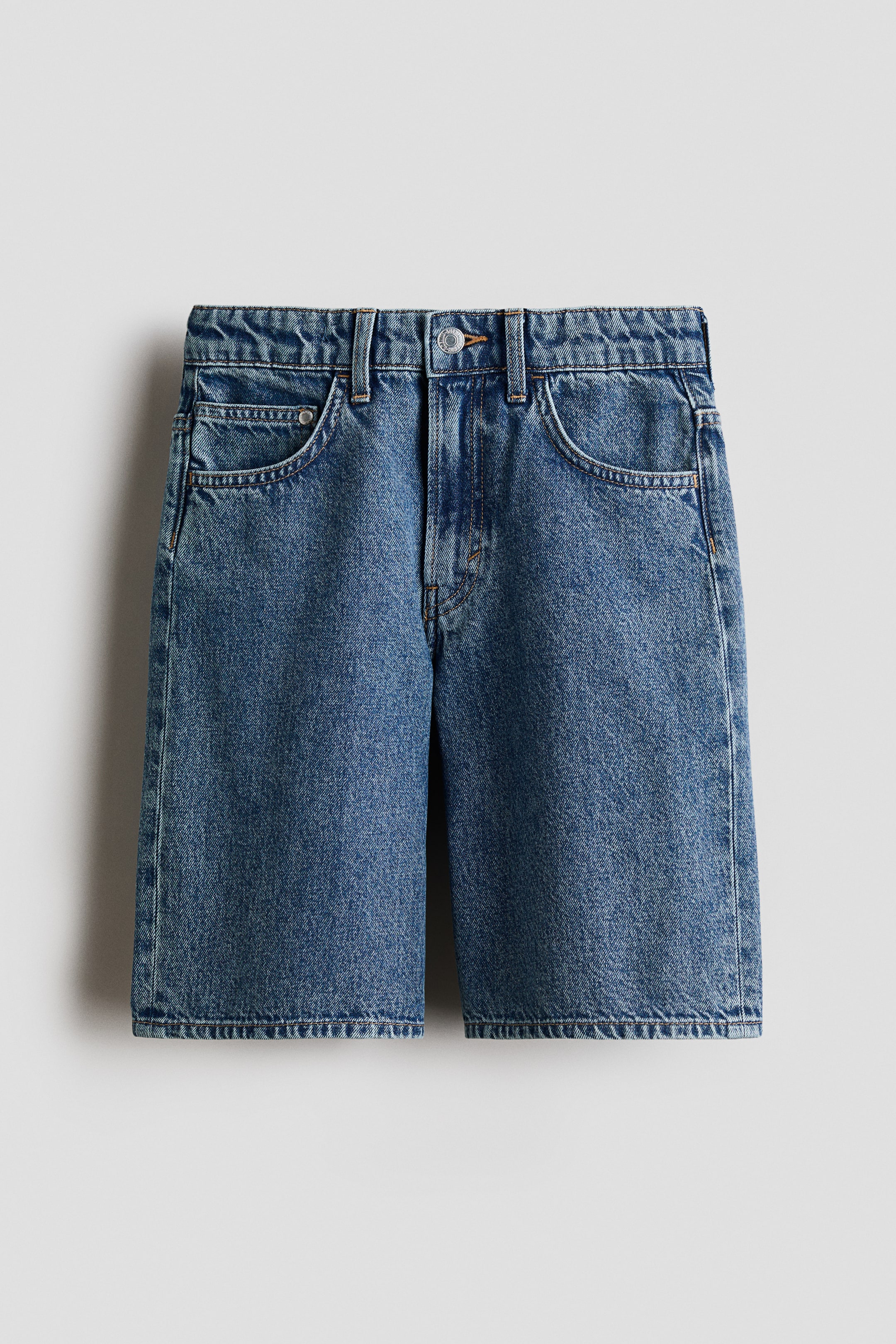 Voir une image plus grande: Les shorts en denim sont présentés de face, arborant une couleur bleu moyen délavé et apparaissant à hauteur du genou. Ils présentent une coupe décontractée, une ceinture avec passants, deux poches avant en biais, une poche à monnaie, et une fermeture éclair avec un bouton.