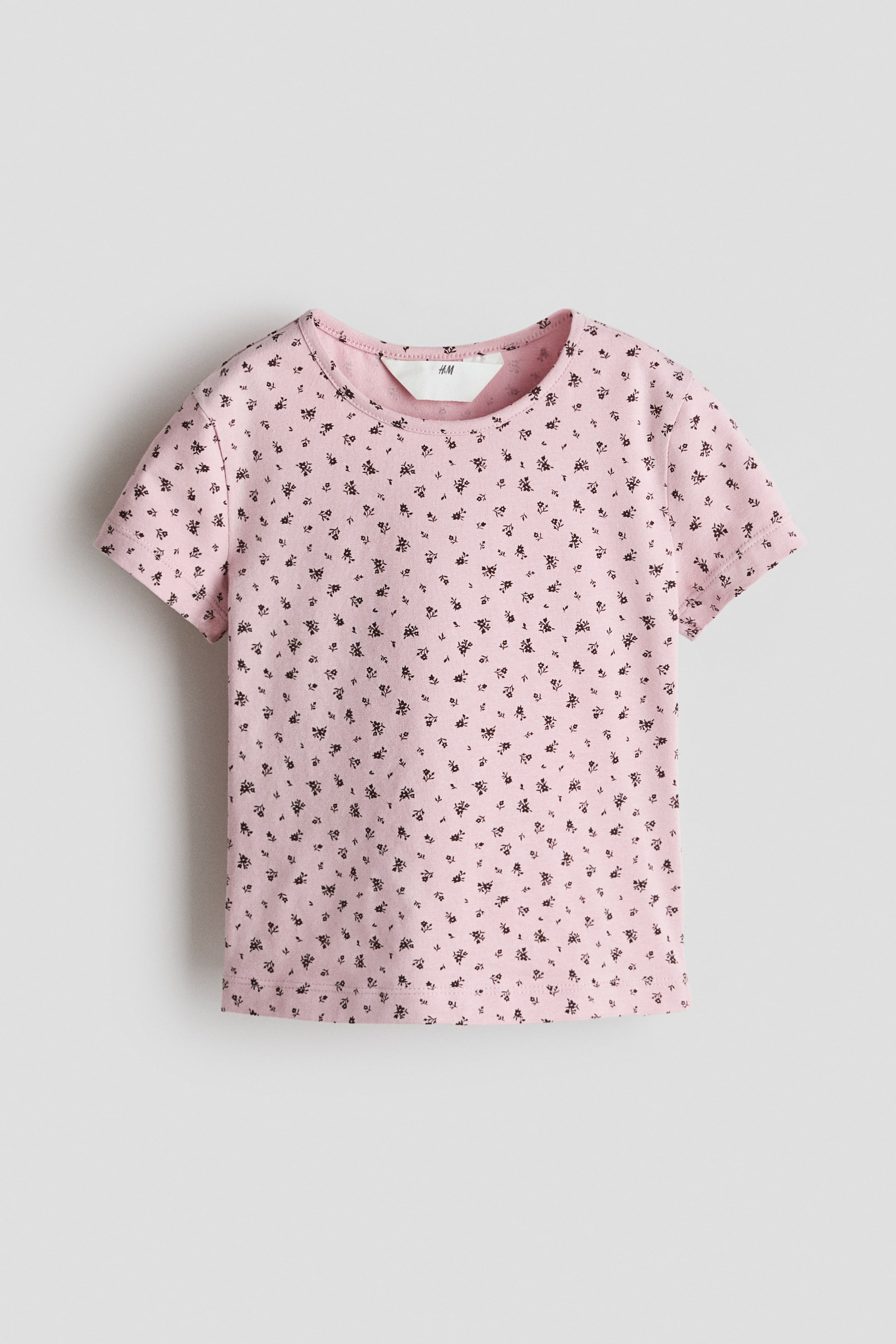 View larger image: A pink t-shirt showcases a subtle dark floral print all over, visible from the front. It features a round neck and short sleeves, with a white brand tag visible on the inner back neckline.