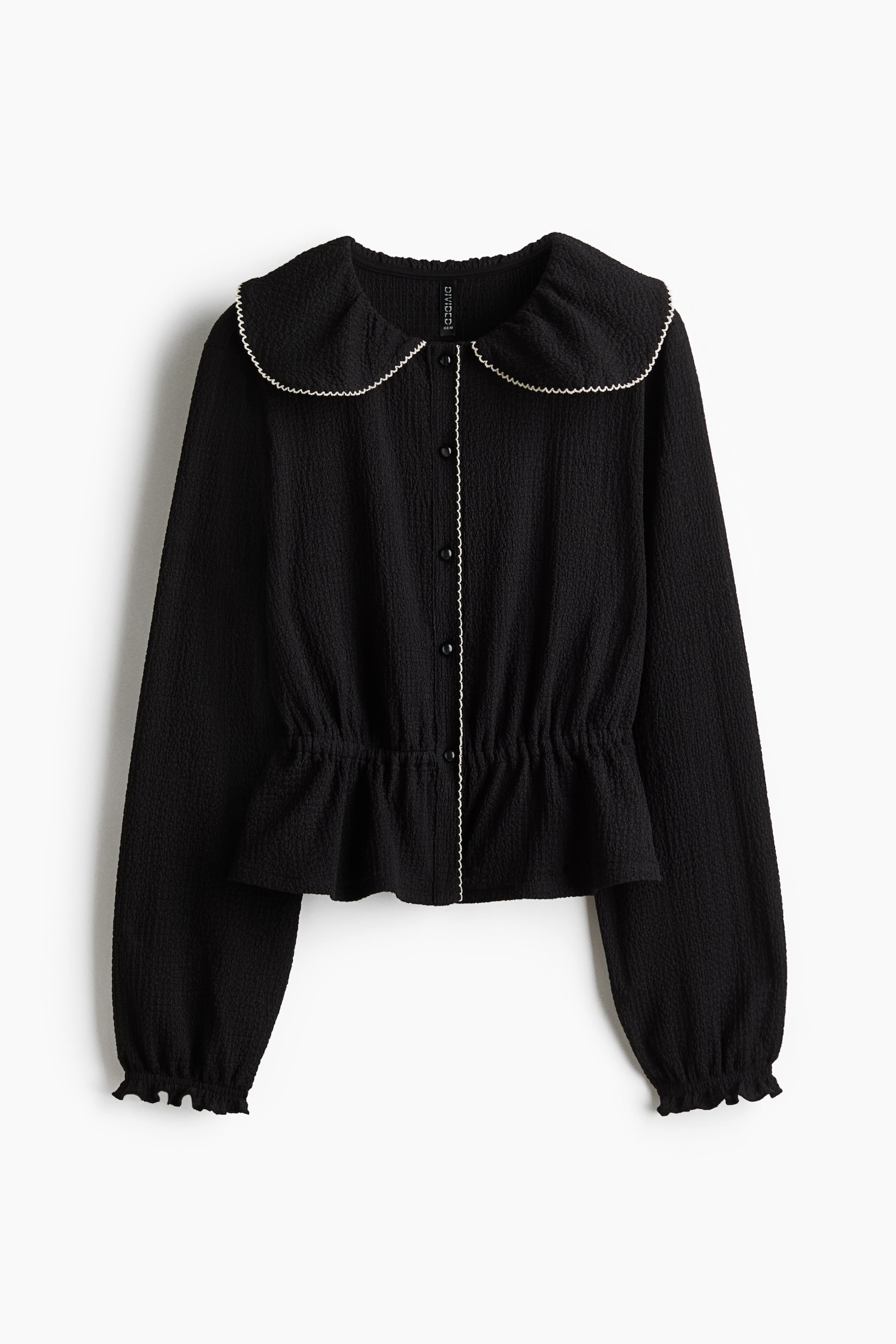 View larger image: A black top shown from the front in textured jersey fabric. It is designed with a picot-trimmed Peter Pan collar, a front button band, long sleeves with elasticated, overlocked cuffs, and a gathered elasticated waist that creates a flared peplum.