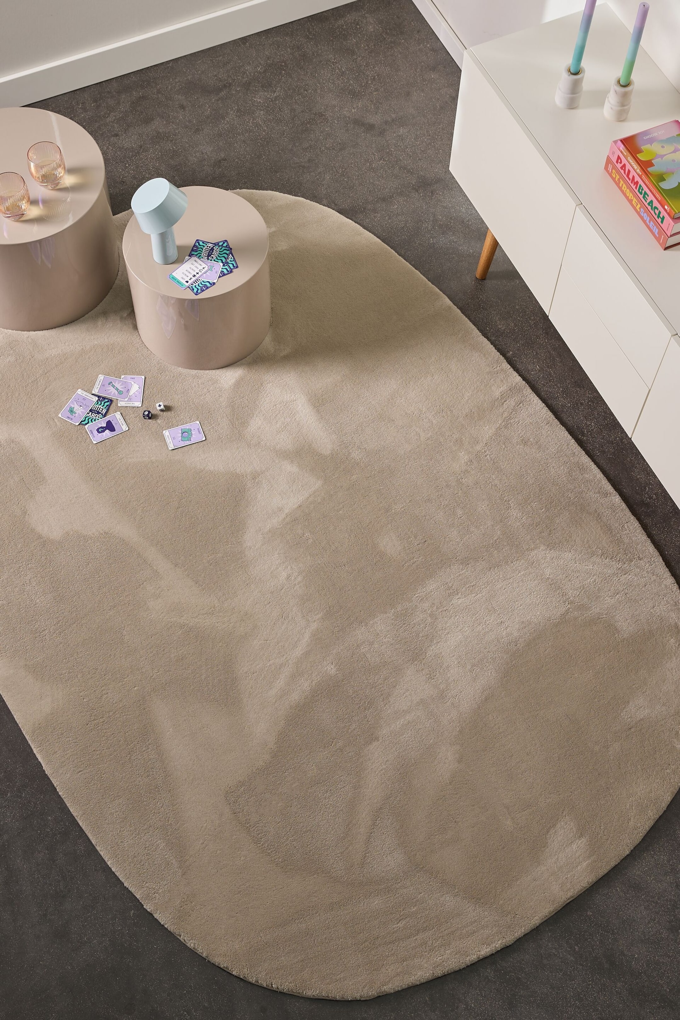 Ver imagen más grande: La alfombra presenta una forma orgánica irregular en color beige claro, con un pelo mullido y sutiles variaciones tonales. Su superficie se extiende bajo dos mesas auxiliares redondas.
