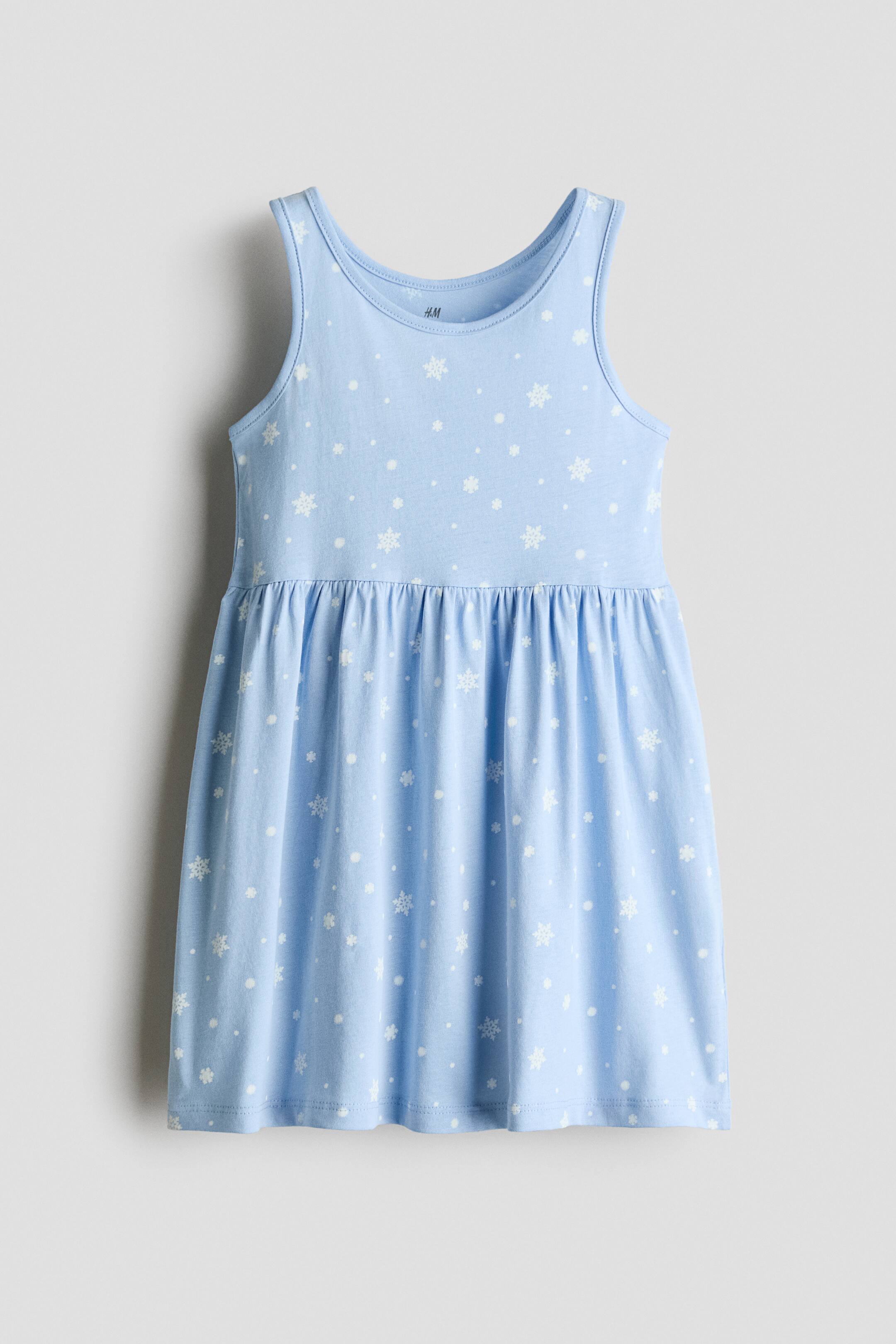 View larger image: A light blue sleeveless dress is shown from the front, featuring a scoop neckline, a gathered waist, and a flared skirt with an all-over print of white snowflakes and dots.